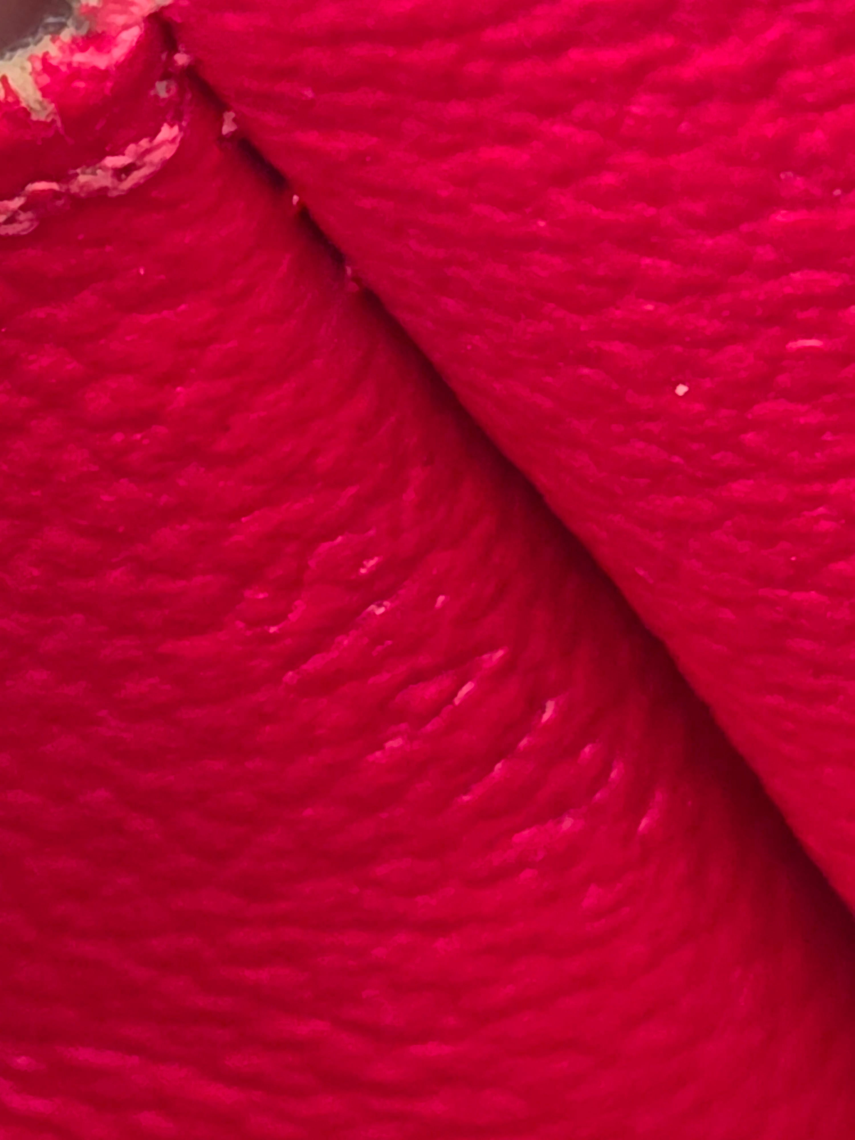 A close-up of bright red textured material, likely leather or faux leather, folded over itself to show the surface texture.