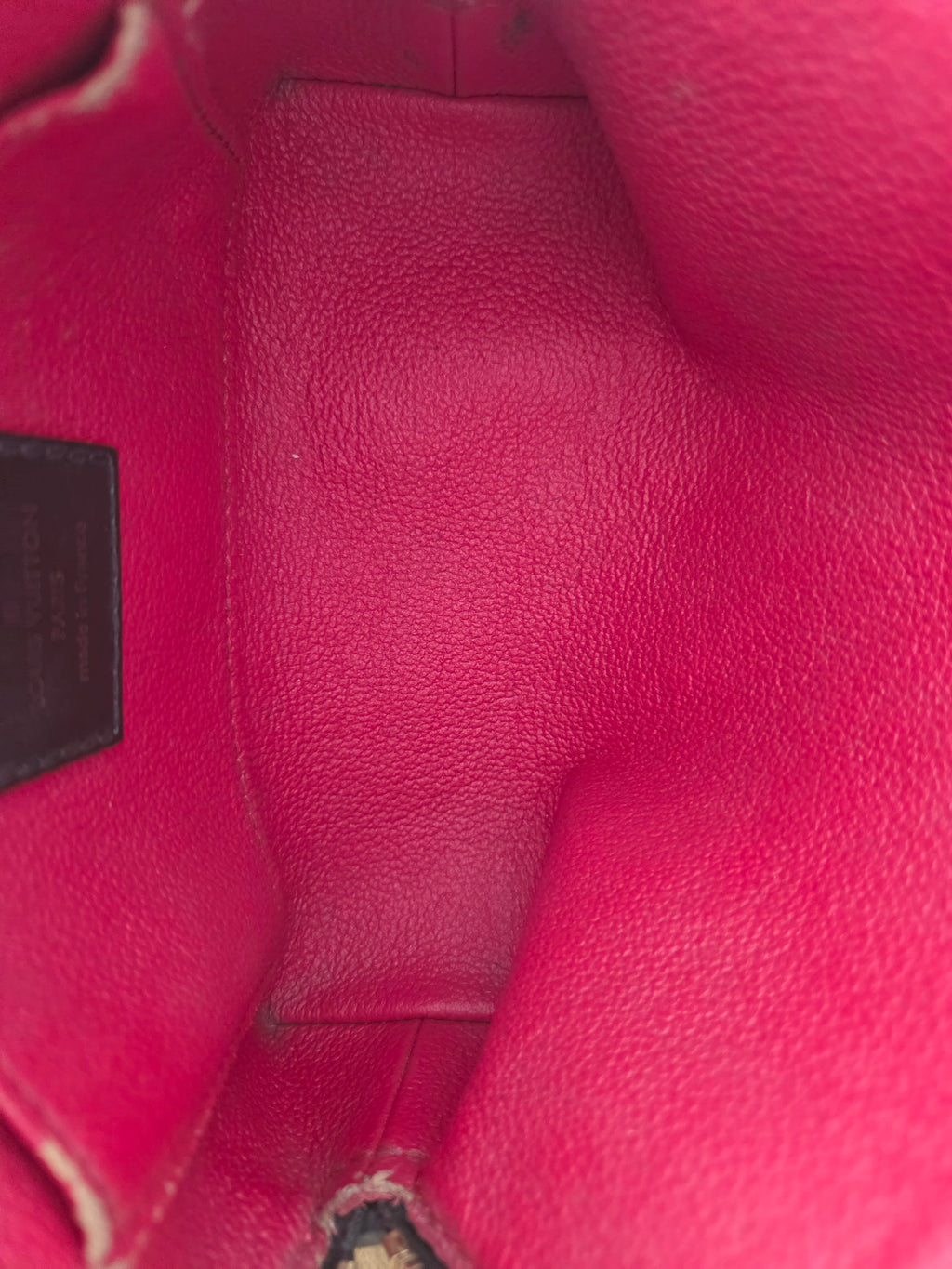 Close-up view of the interior lining of a pink pebbled leather handbag, showing the interior base and a small dark brand plaque near the bottom.