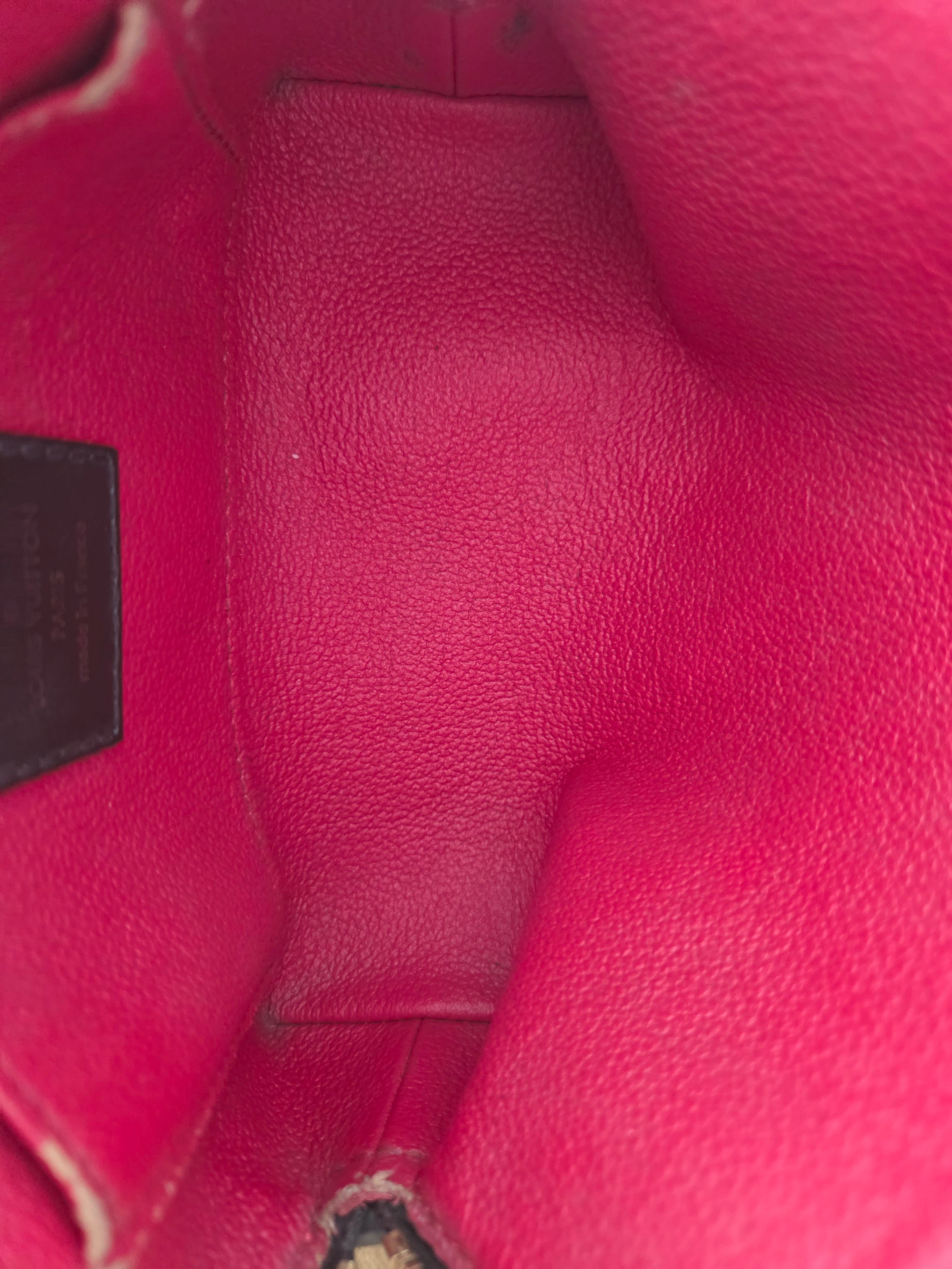Close-up view of the interior lining of a pink pebbled leather handbag, showing the interior base and a small dark brand plaque near the bottom.