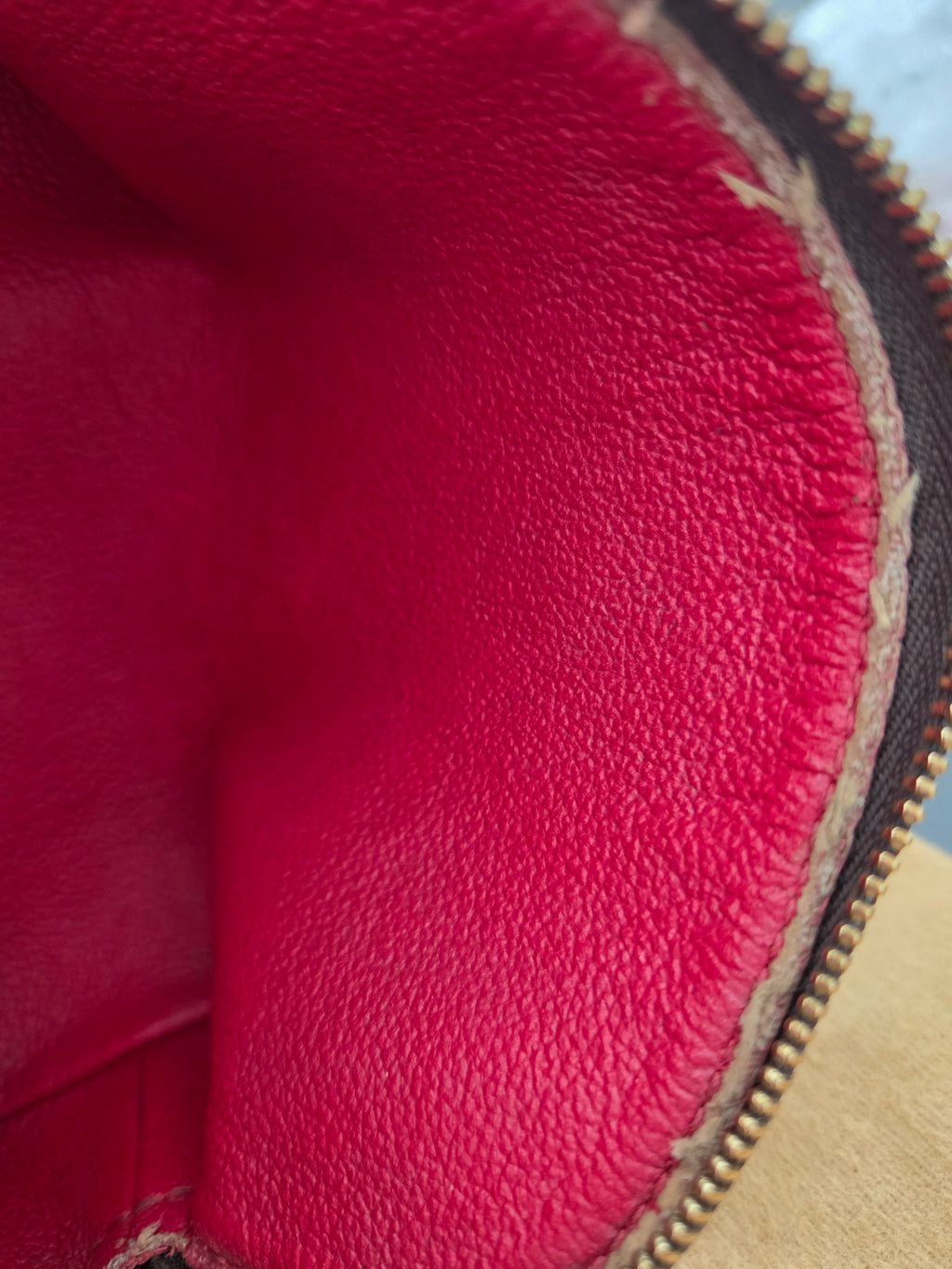 Close-up of a pebbled leather interior in a vibrant pinkish-red color, showing a gold-toned zipper along the top edge.