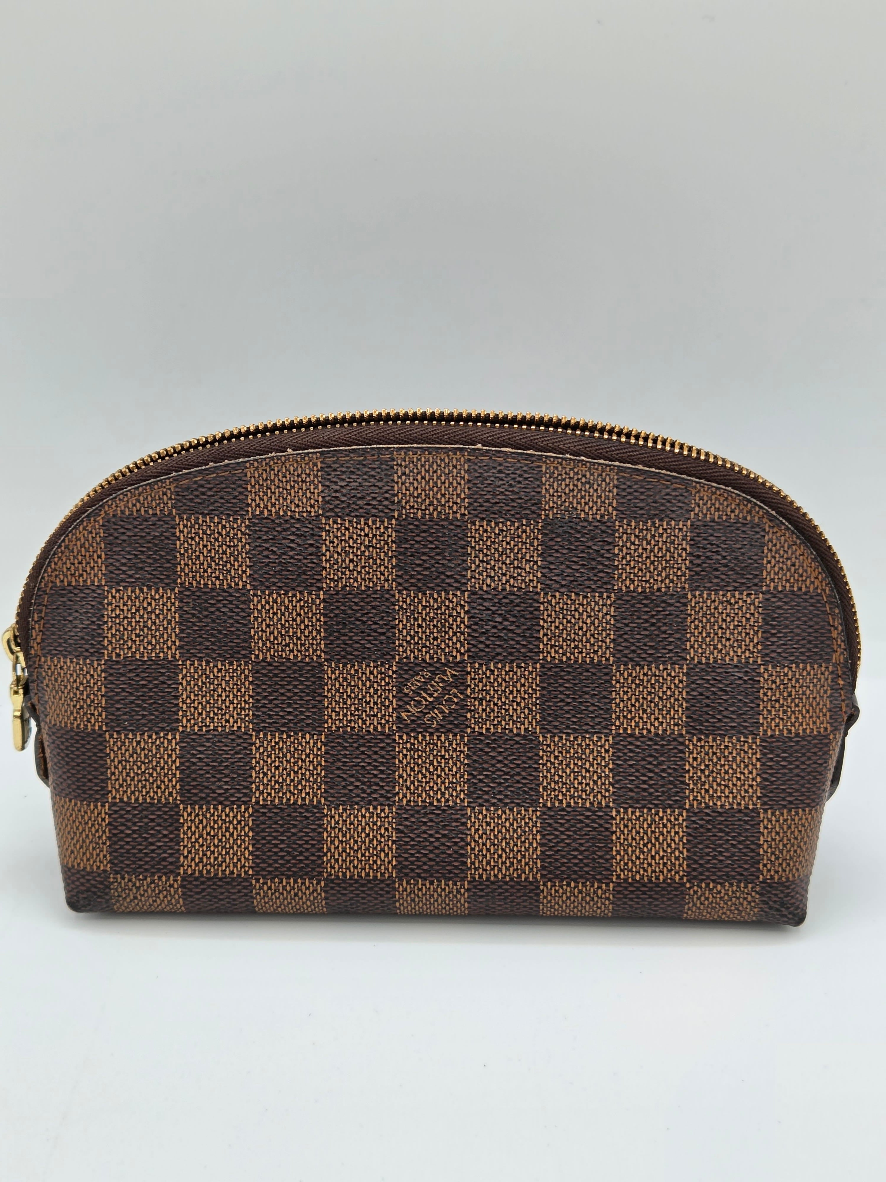 A Louis Vuitton zippered pouch in the Damier Ebene checkered canvas, featuring alternating brown and tan squares with a gold-tone zipper.