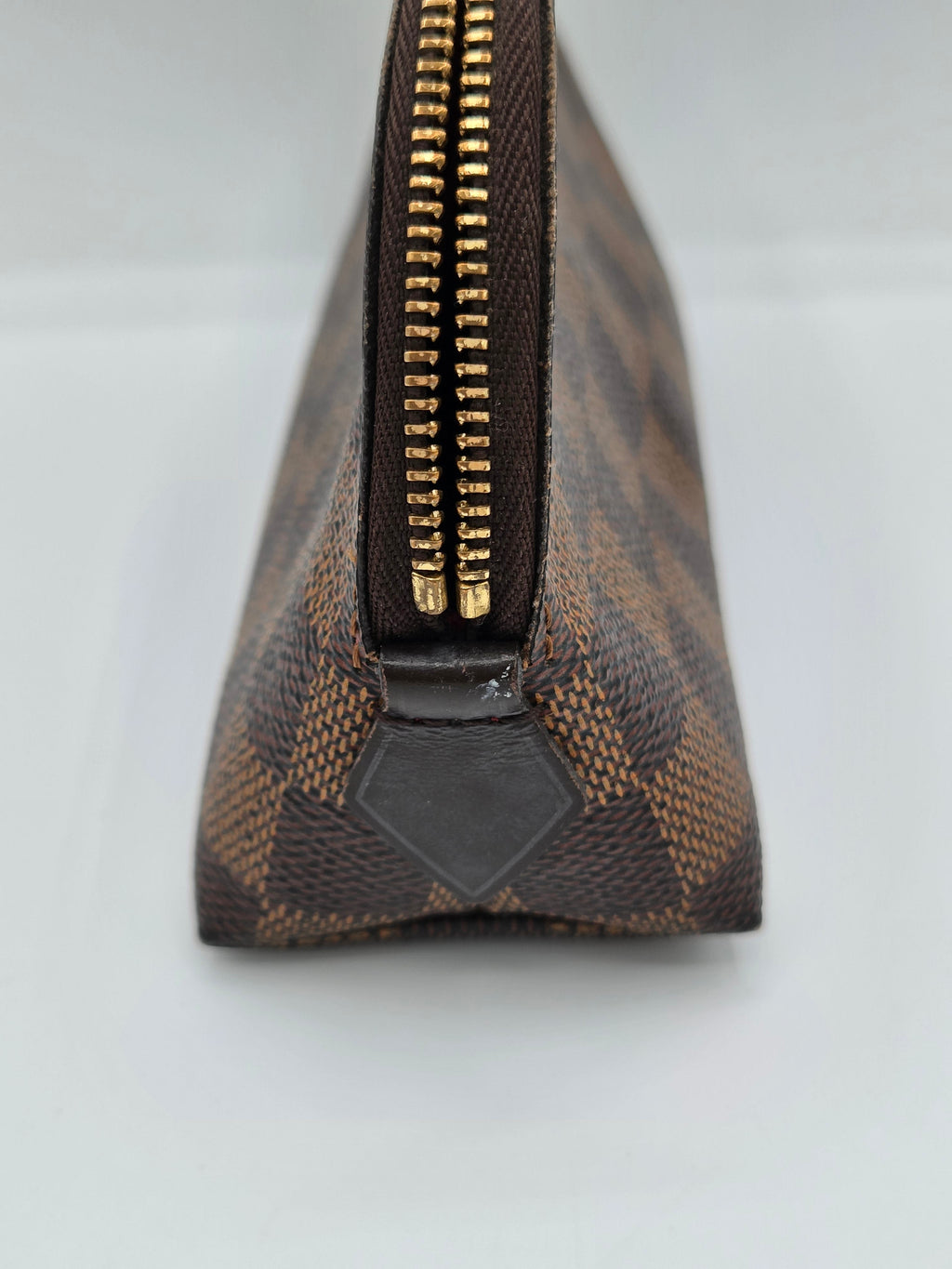A close-up of a brown and beige checkered leather pouch with a gold zipper and a black diamond-shaped leather tab.