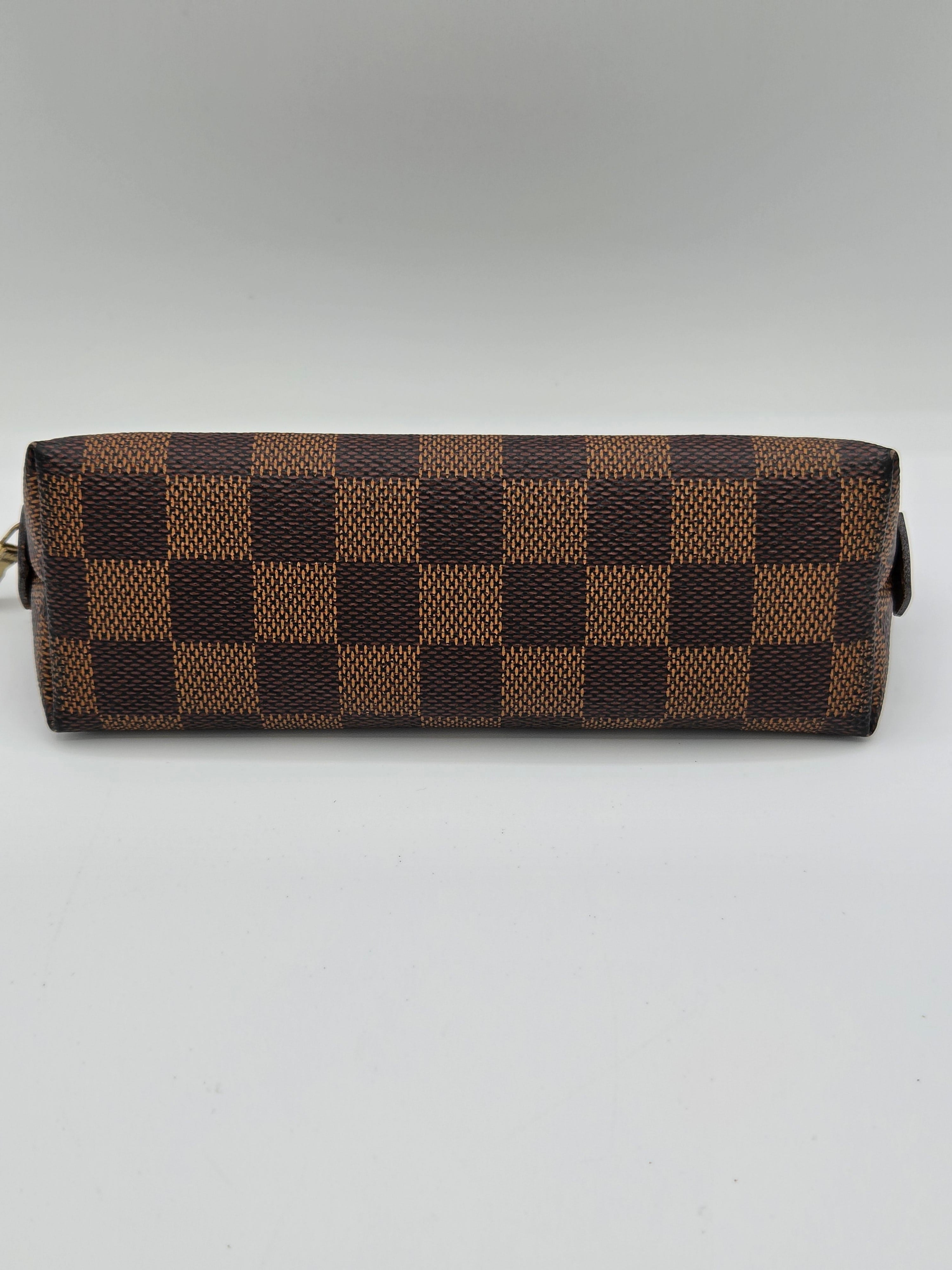 A Louis Vuitton monogram pouch in brown and beige Damier Ebene canvas, shown vertically against a light gray background.