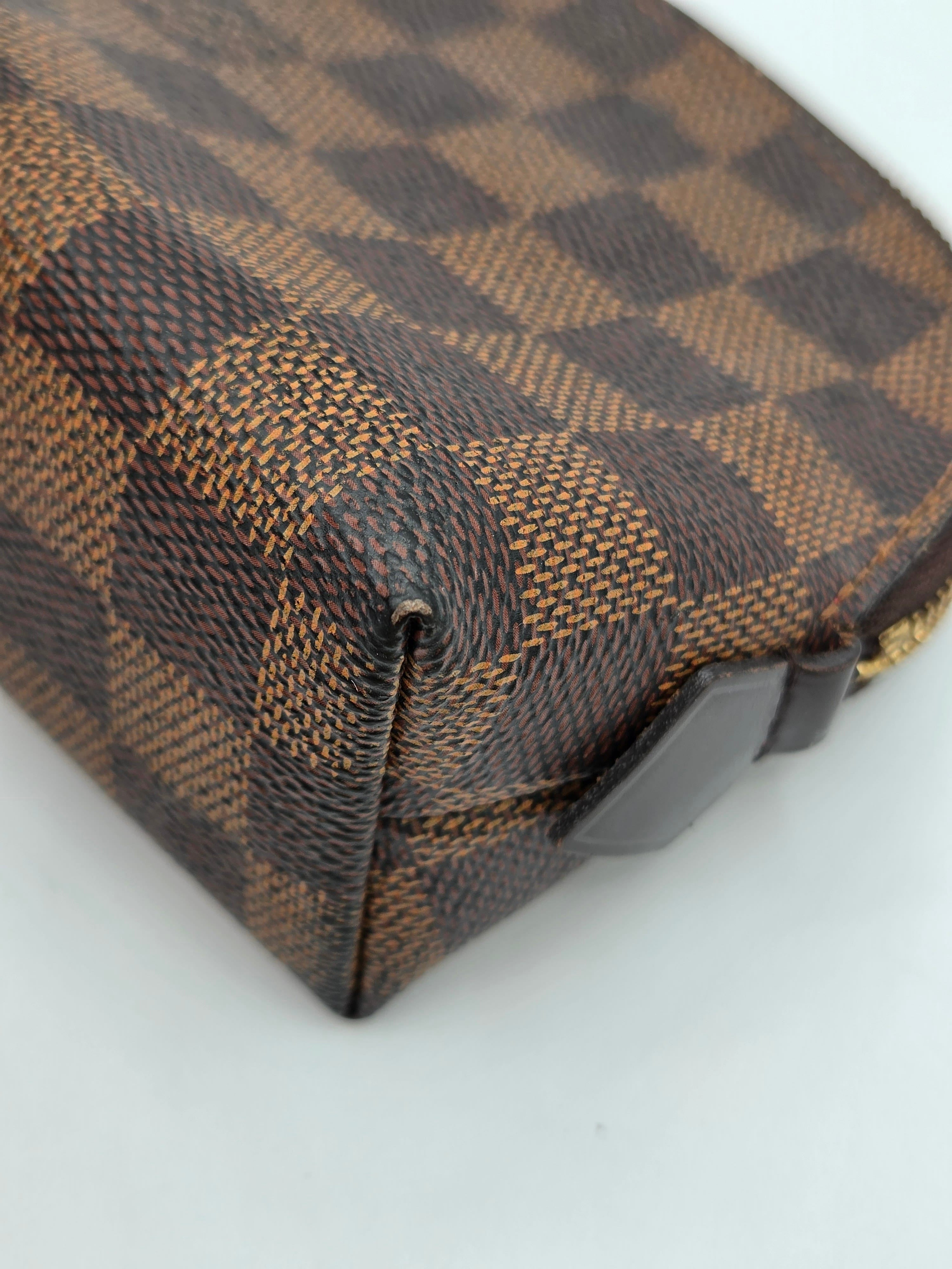 Close-up of a brown and beige checkerboard patterned leather pouch with a dark brown zipper tab, on a plain white background.