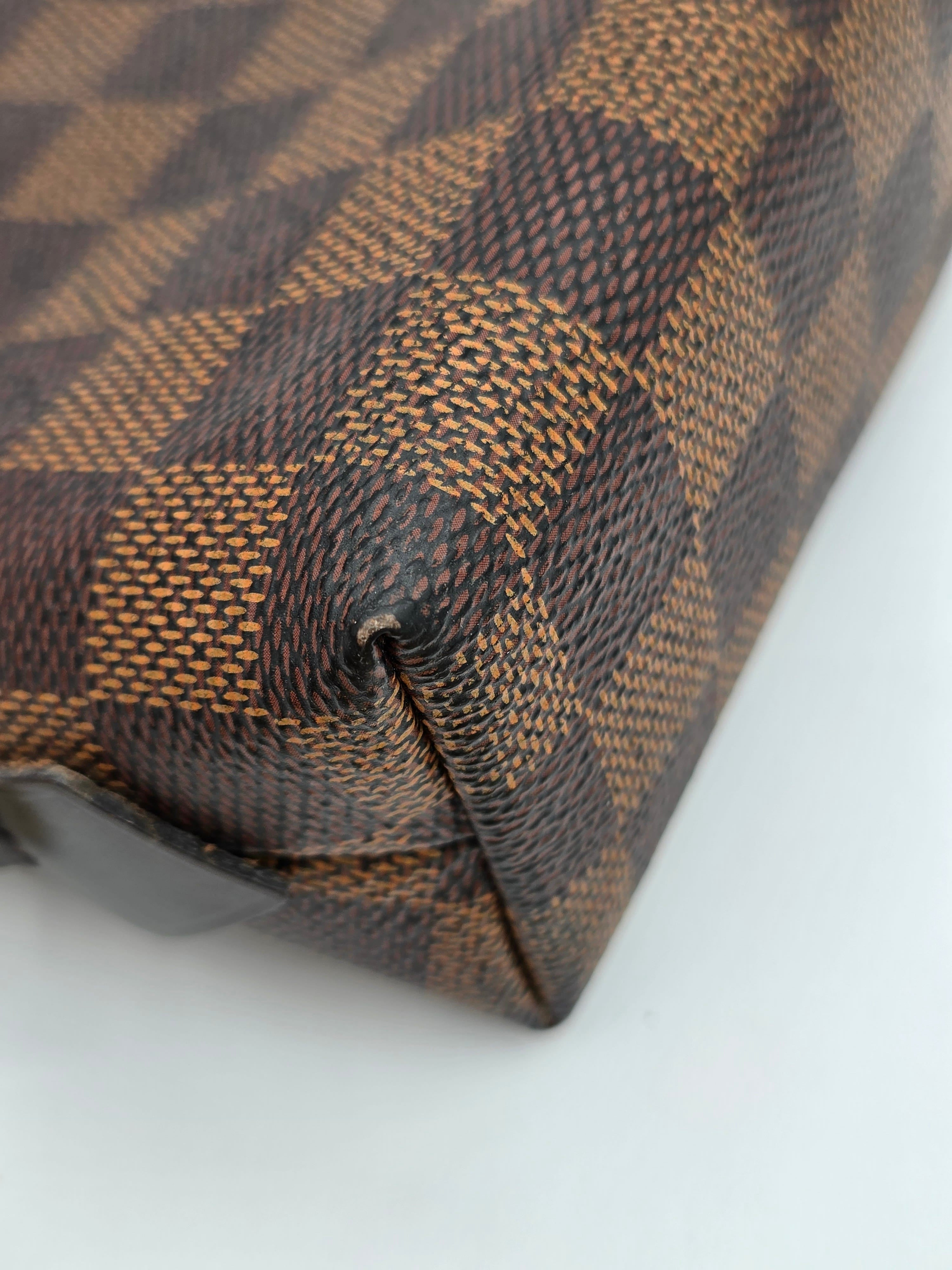 Close-up of a brown and beige checkered canvas bag corner showing the textured woven pattern and stitched edge against a plain light background.