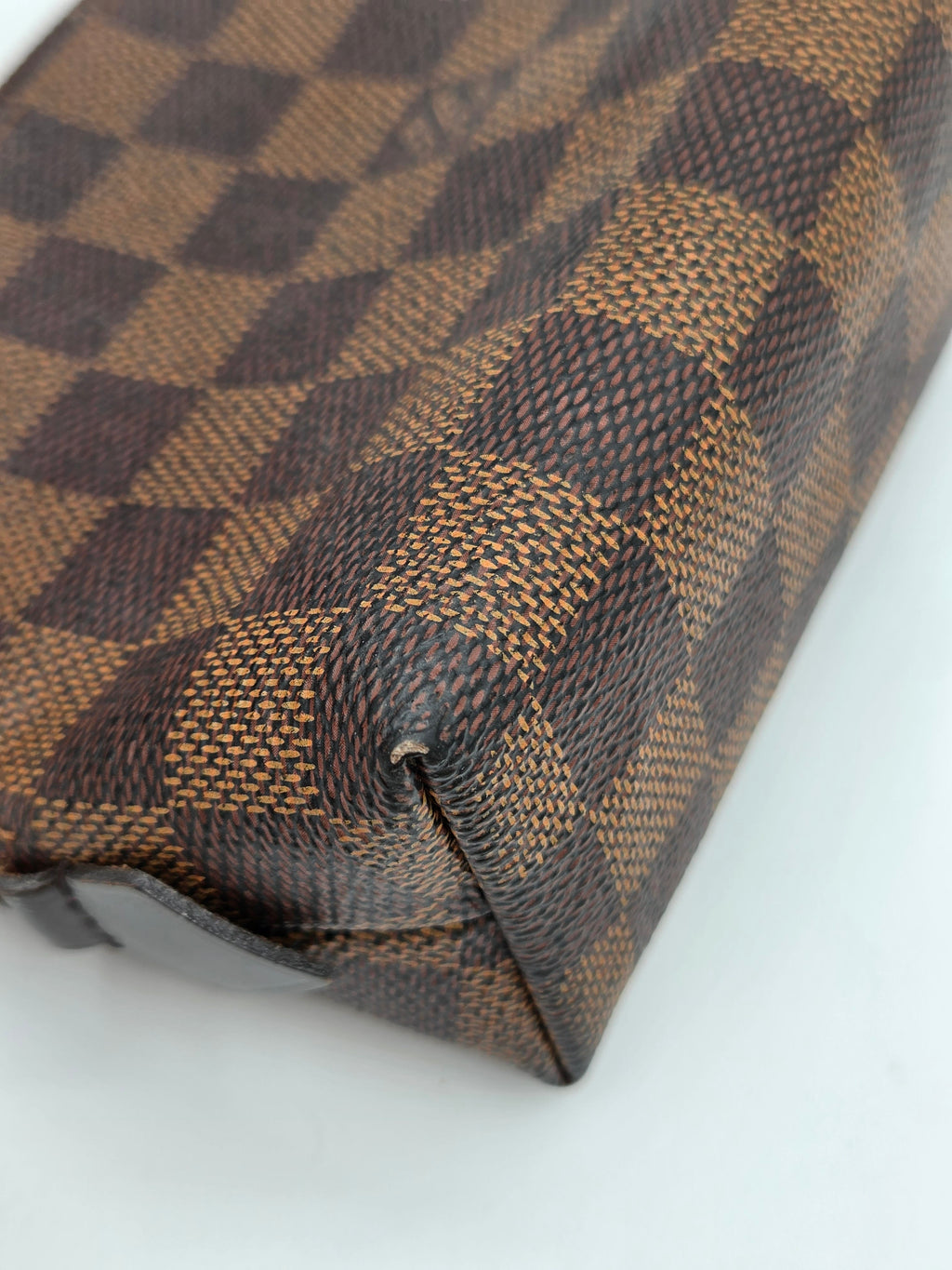 A close-up of a brown and beige checkerboard patterned leather pouch, showing the textured canvas weave and a dark brown leather edge against a plain white background.
