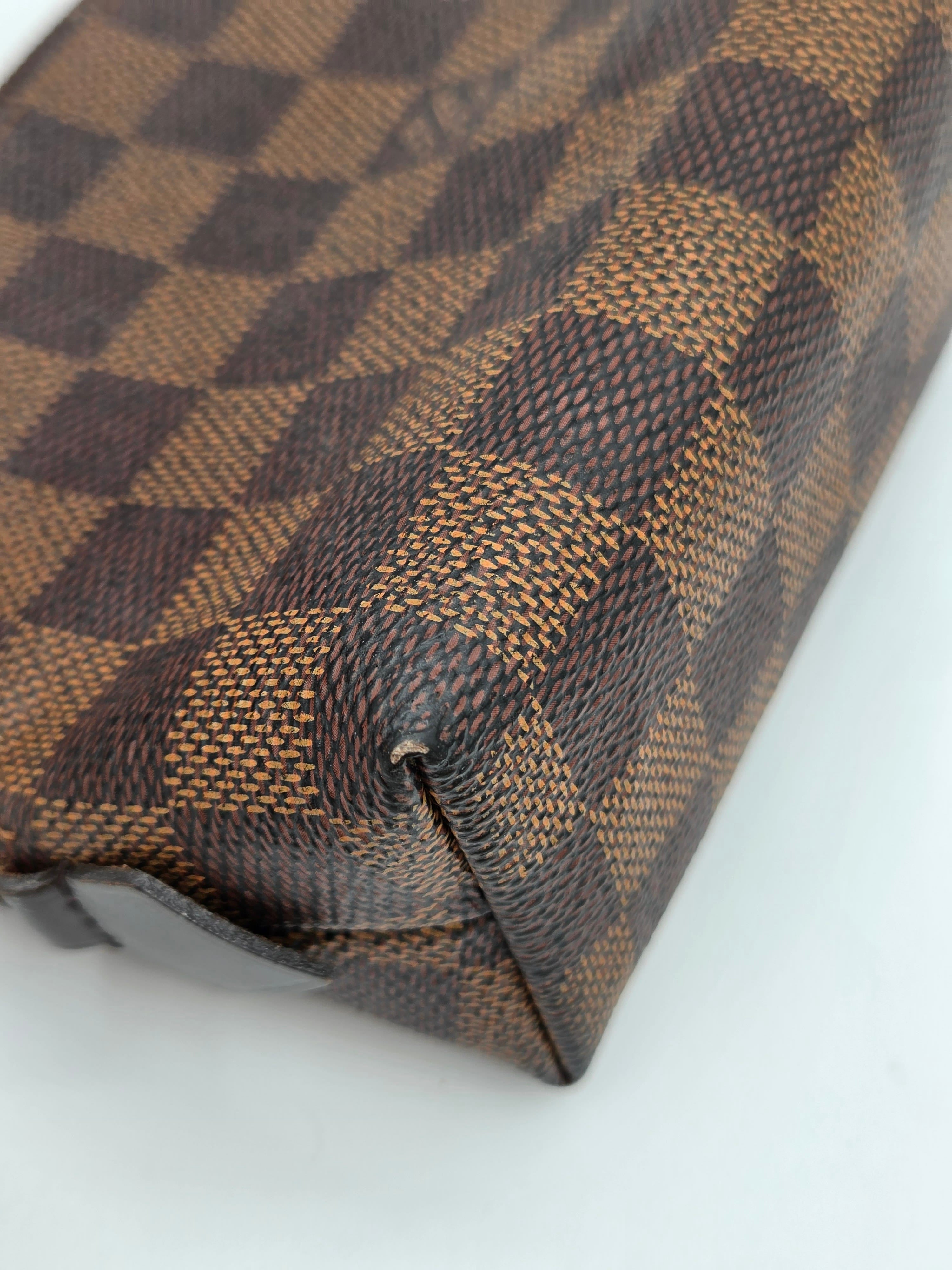 A close-up of a brown and beige checkerboard patterned leather pouch, showing the textured canvas weave and a dark brown leather edge against a plain white background.