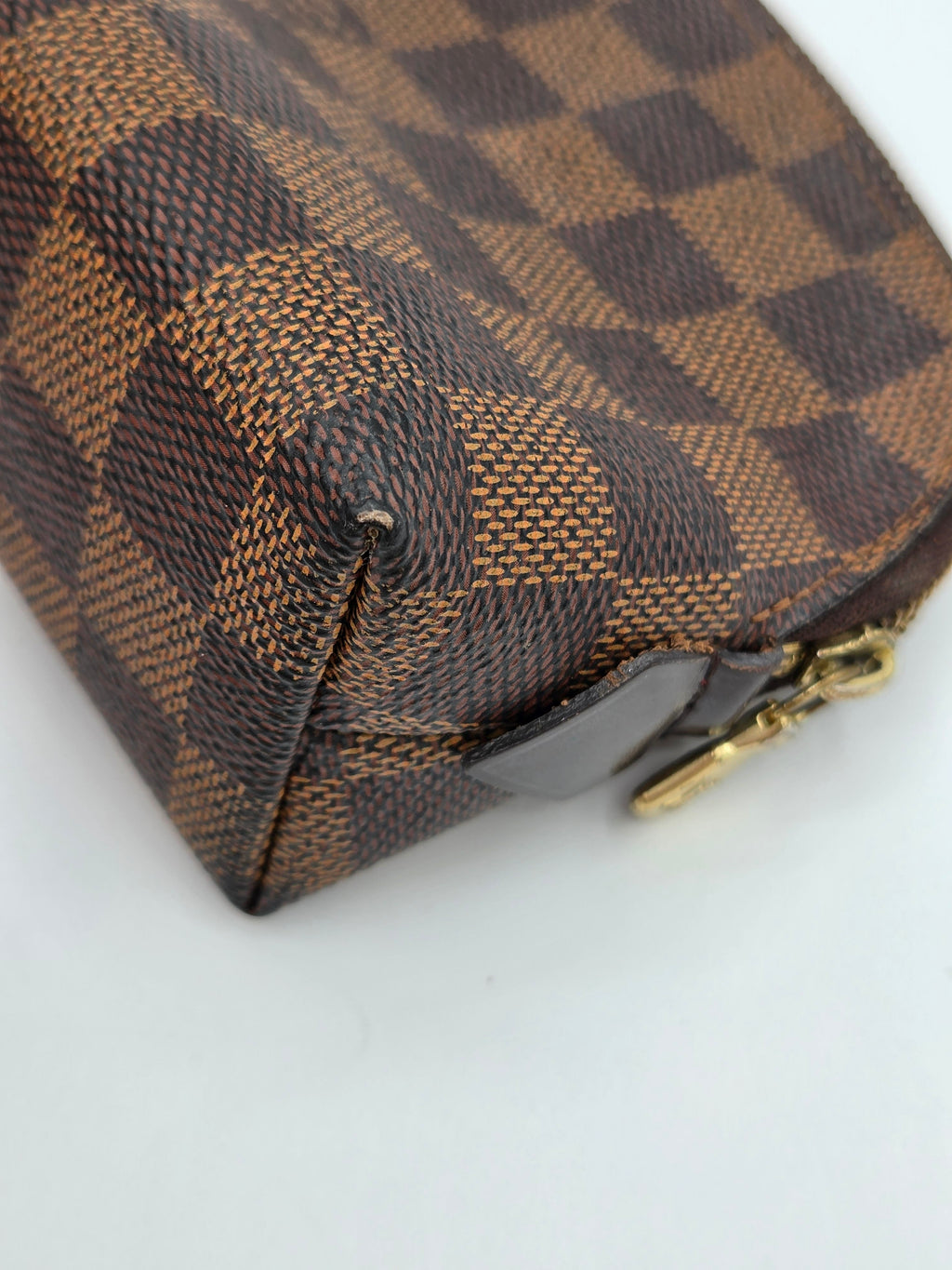 A close-up of a brown and tan checkered canvas pouch with a gold zipper pull, showing the textured pattern and corner detail against a plain white background.