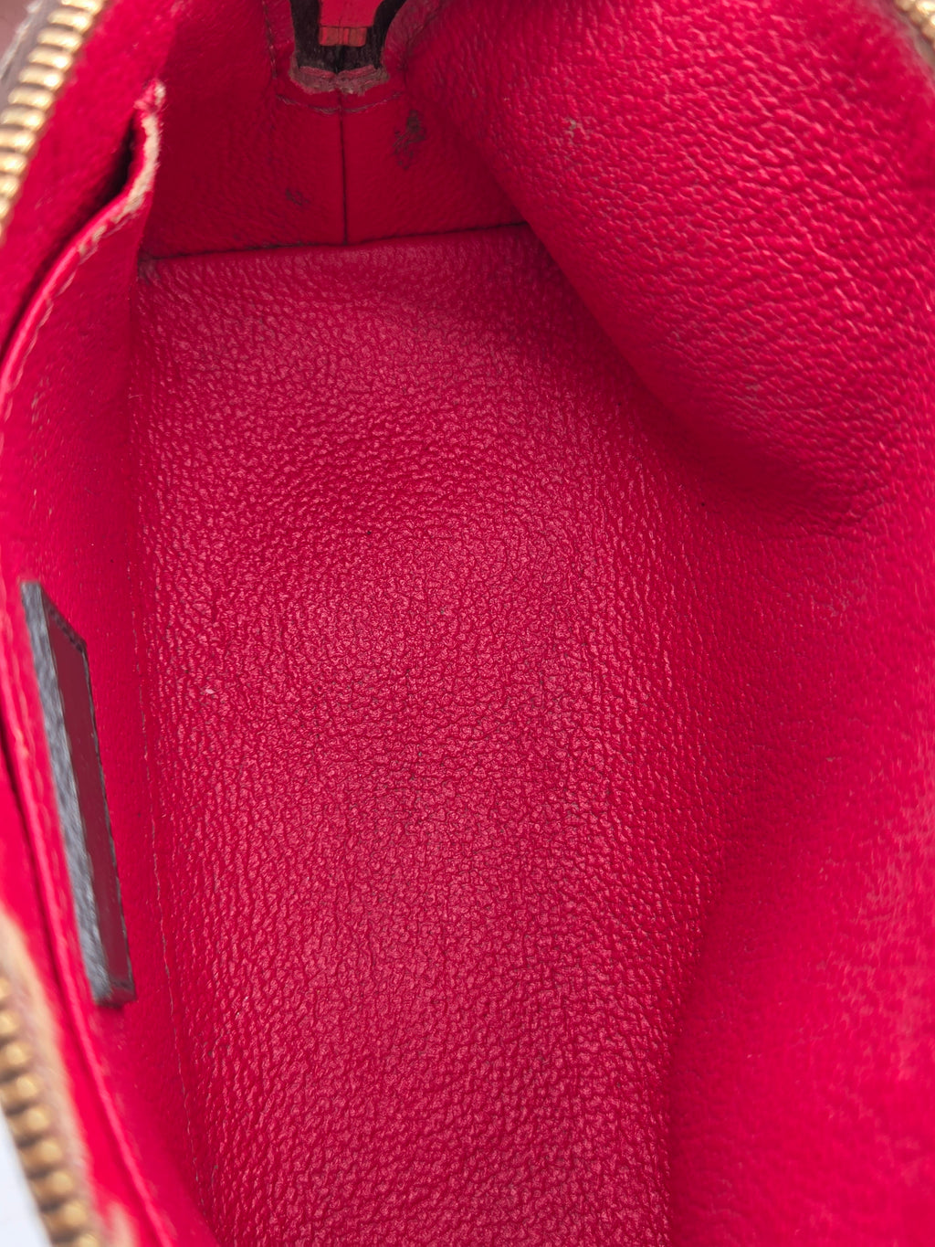 Close-up of the interior lining of a red textured leather pouch or clutch, showing the pebbled leather texture and a gold zipper edge at the bottom.