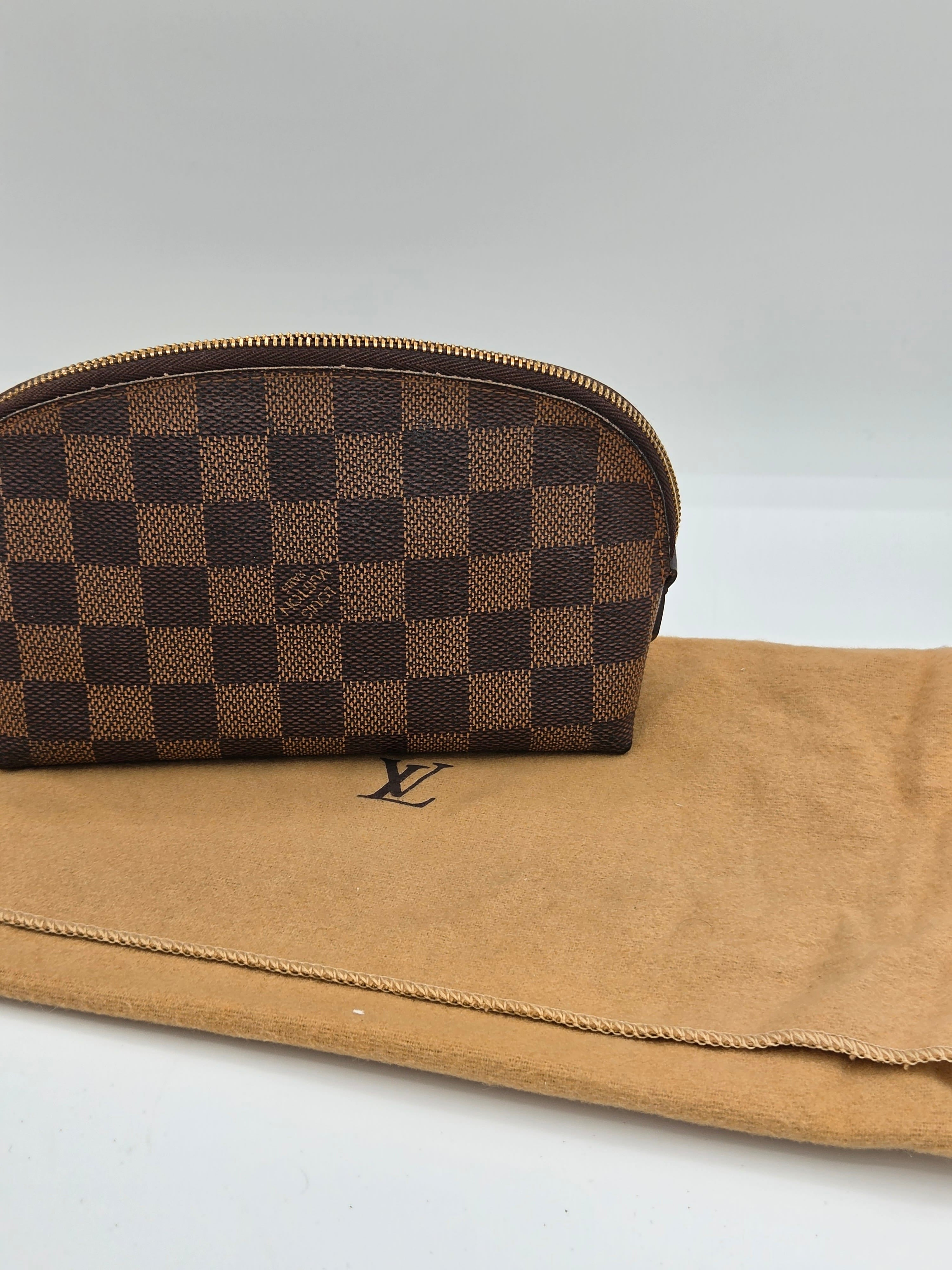 A Louis Vuitton zippered pouch in the classic Damier Ebene checkered pattern, shown next to its tan suede dust bag against a plain white background.