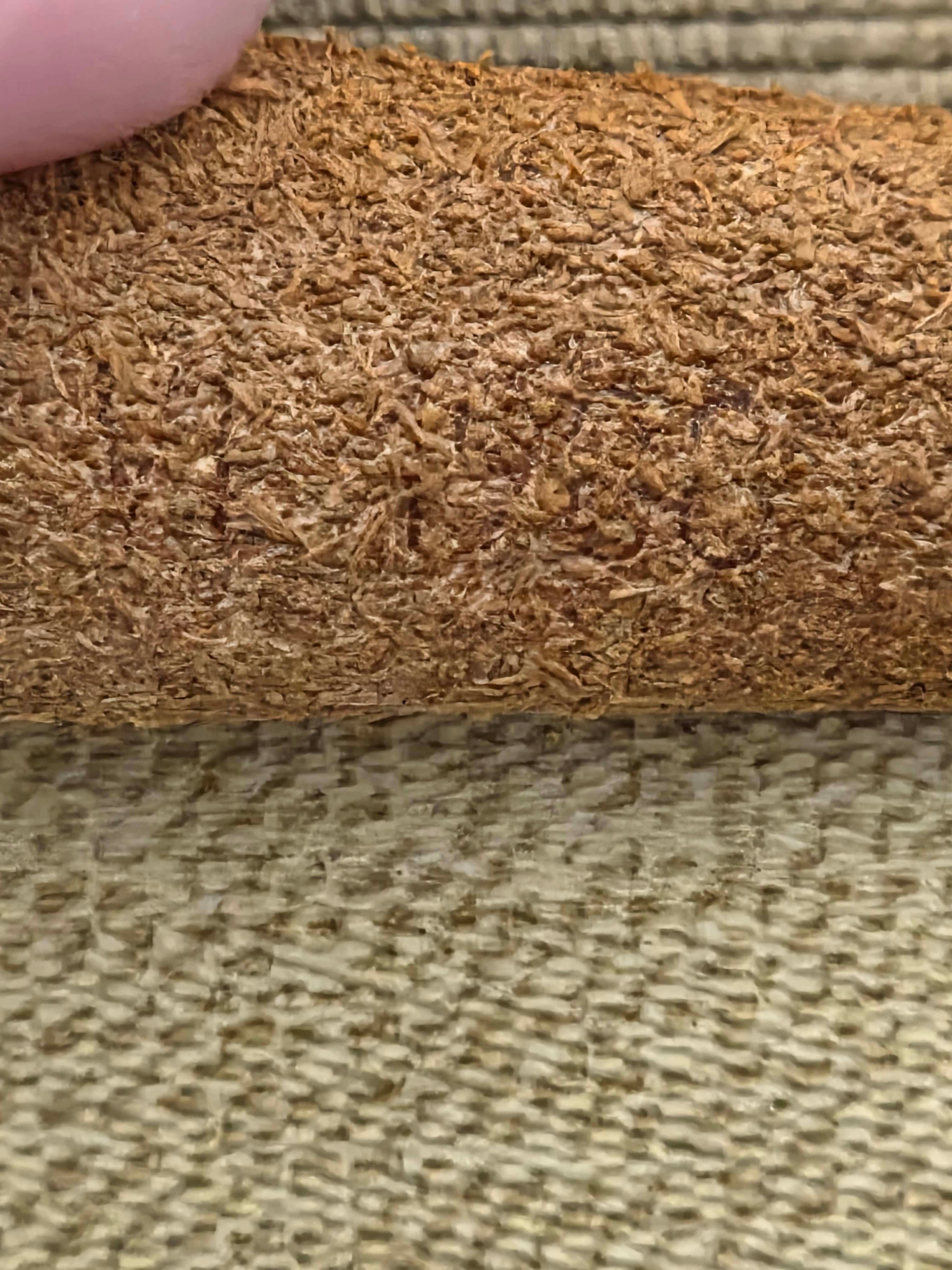 A close-up of a textured brown material, likely a leather or suede roll, held by a finger against a woven beige background.