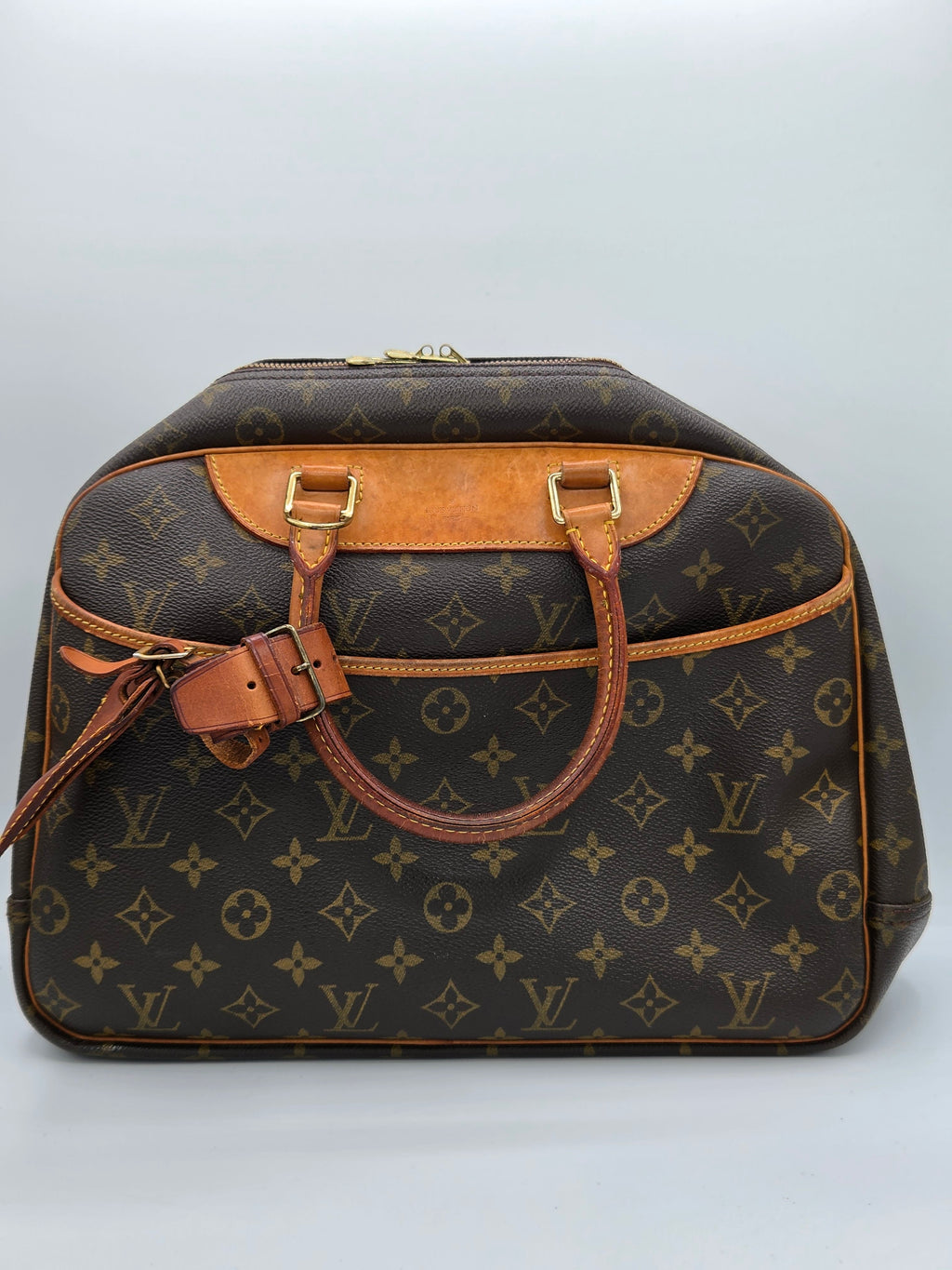 A Louis Vuitton monogram canvas handbag with tan leather trim and gold-tone hardware, photographed from an overhead angle against a light gray background.