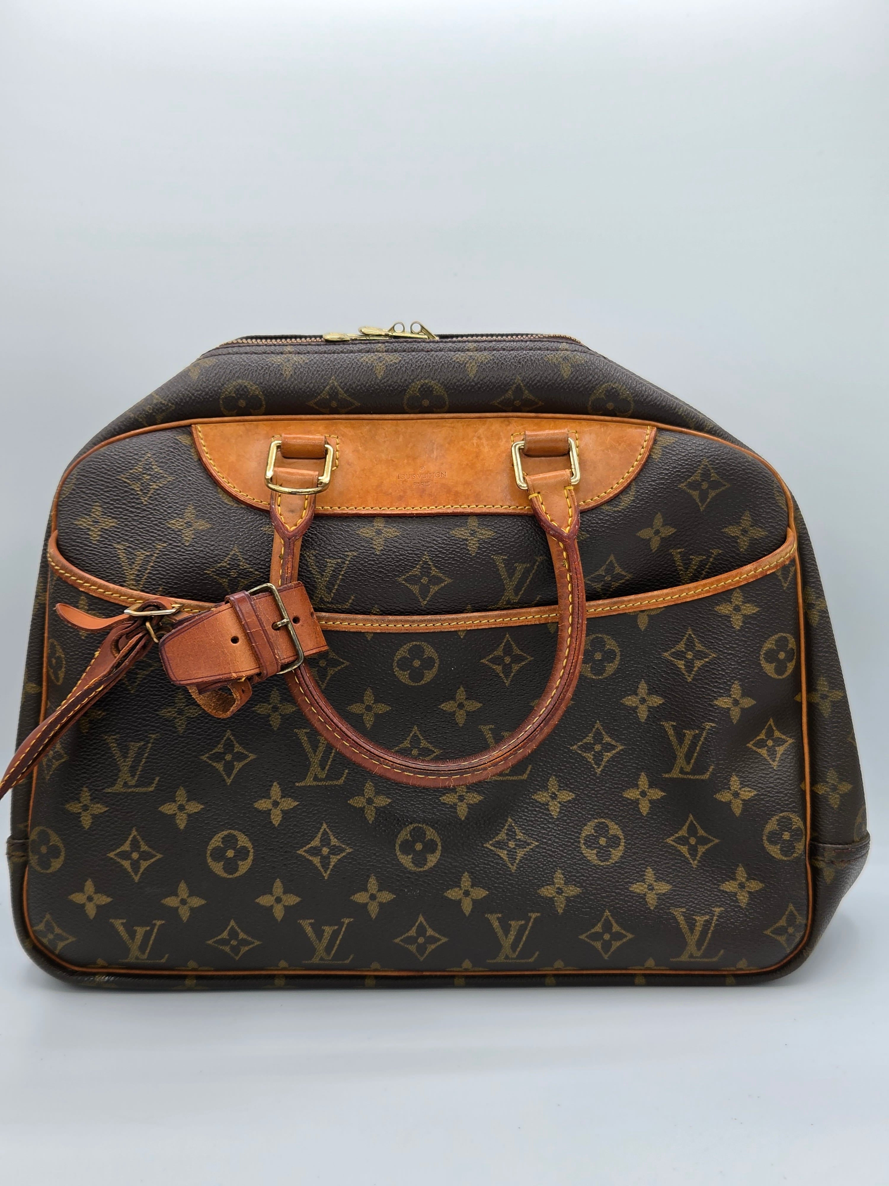 A Louis Vuitton monogram canvas handbag with tan leather trim and gold-tone hardware, photographed from an overhead angle against a light gray background.