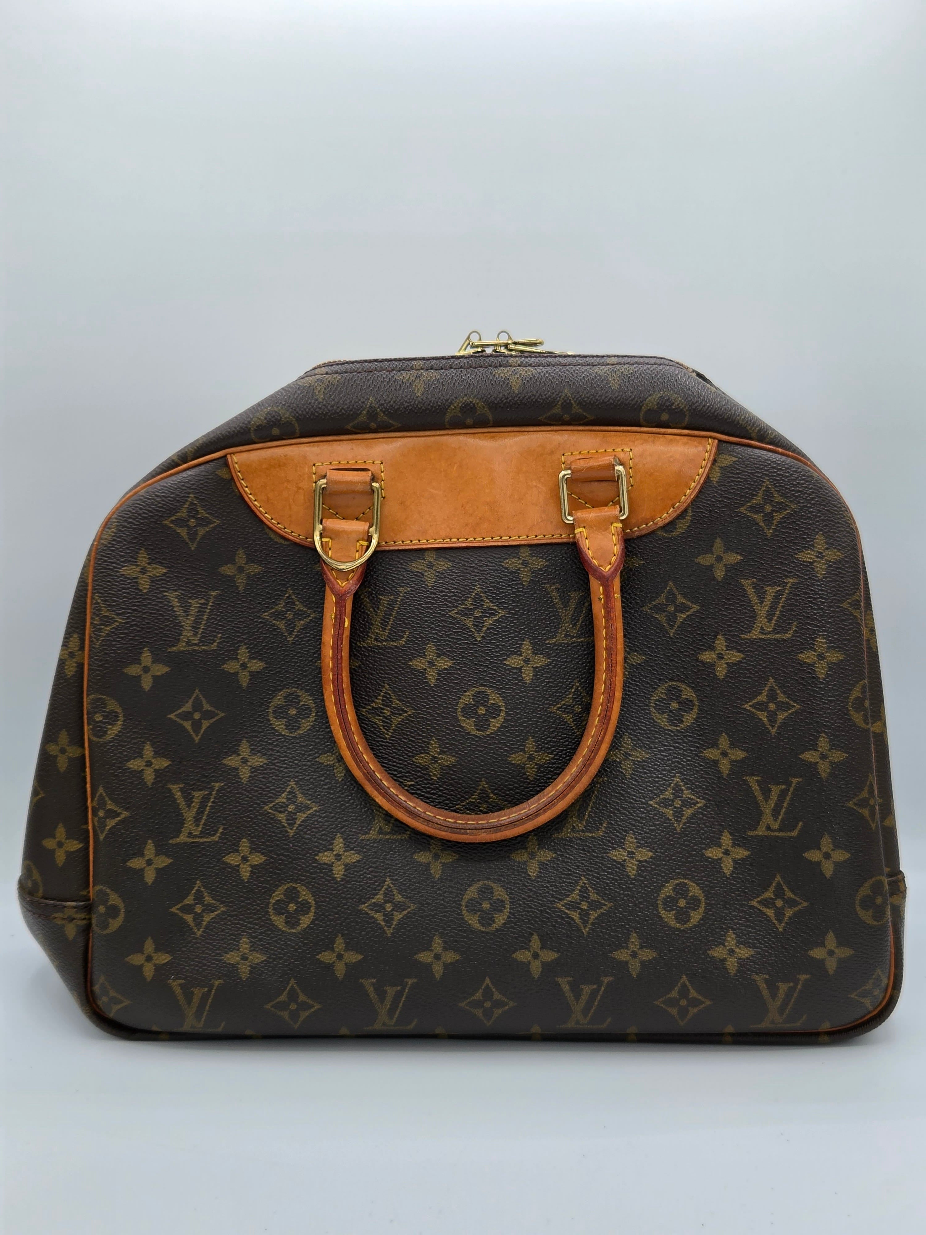 Louis Vuitton monogram canvas Speedy bag with tan leather handles and trim, gold-tone hardware, and a zip-top closure, photographed against a light gray studio background.