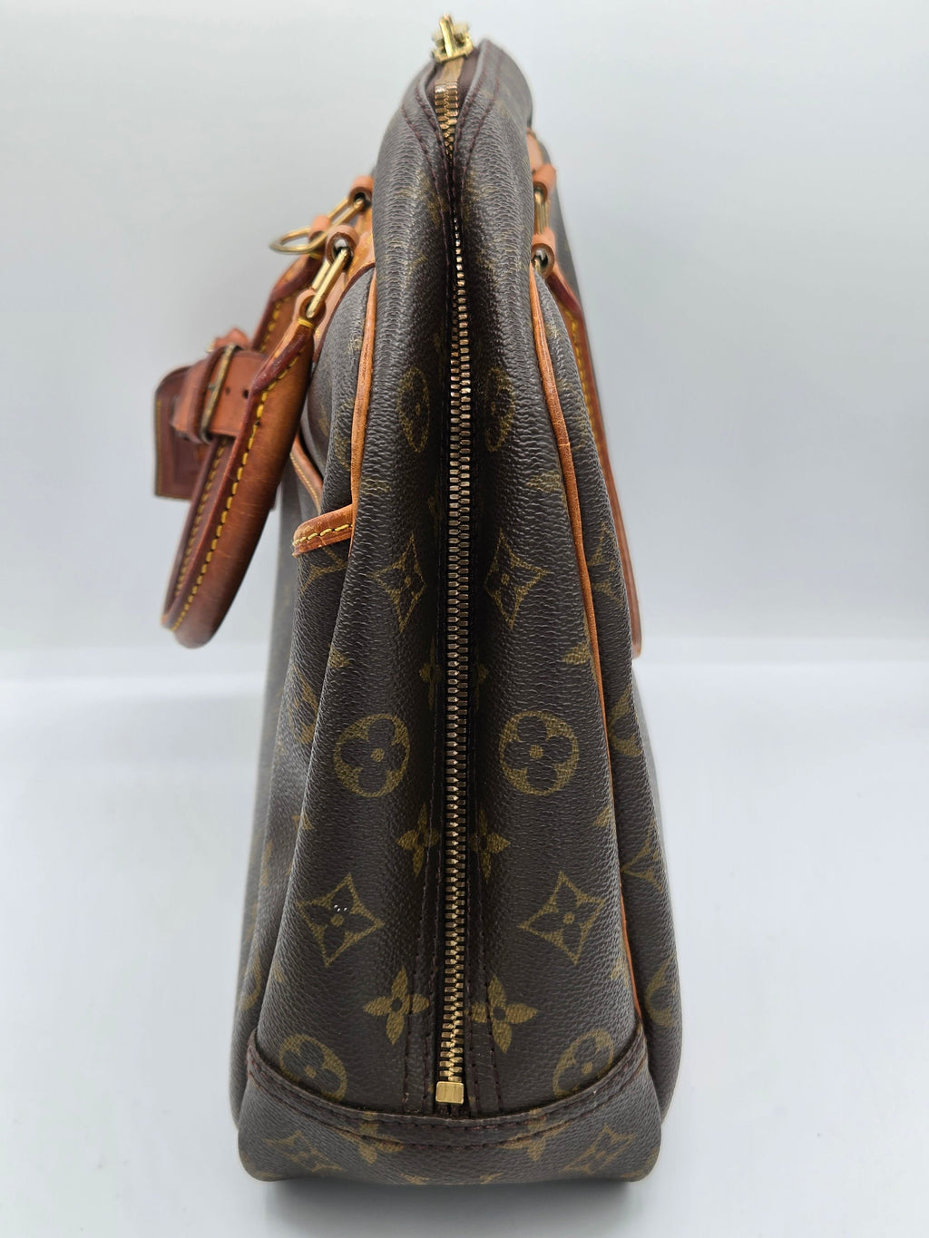A Louis Vuitton monogram canvas handbag shown from a side profile view, featuring the classic dark brown and tan pattern with gold-tone hardware.