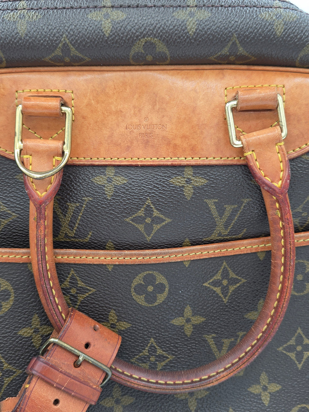 Close-up of a Louis Vuitton handbag showing the brown monogram canvas and tan leather trim with gold-tone metal hardware.