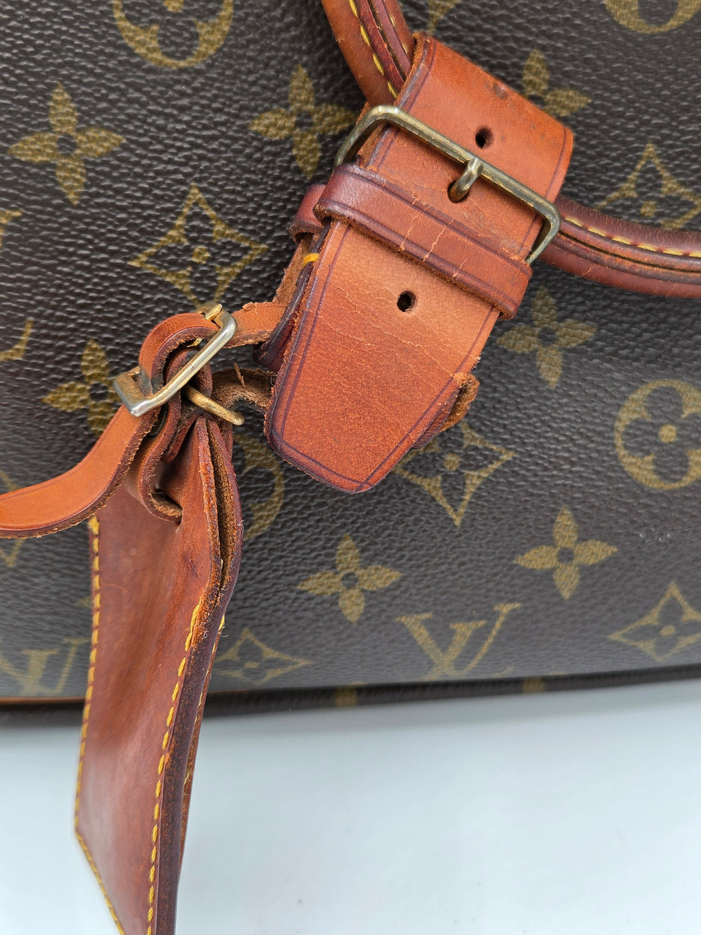 Close-up of a Louis Vuitton monogram canvas bag with brown leather strap and buckle details.