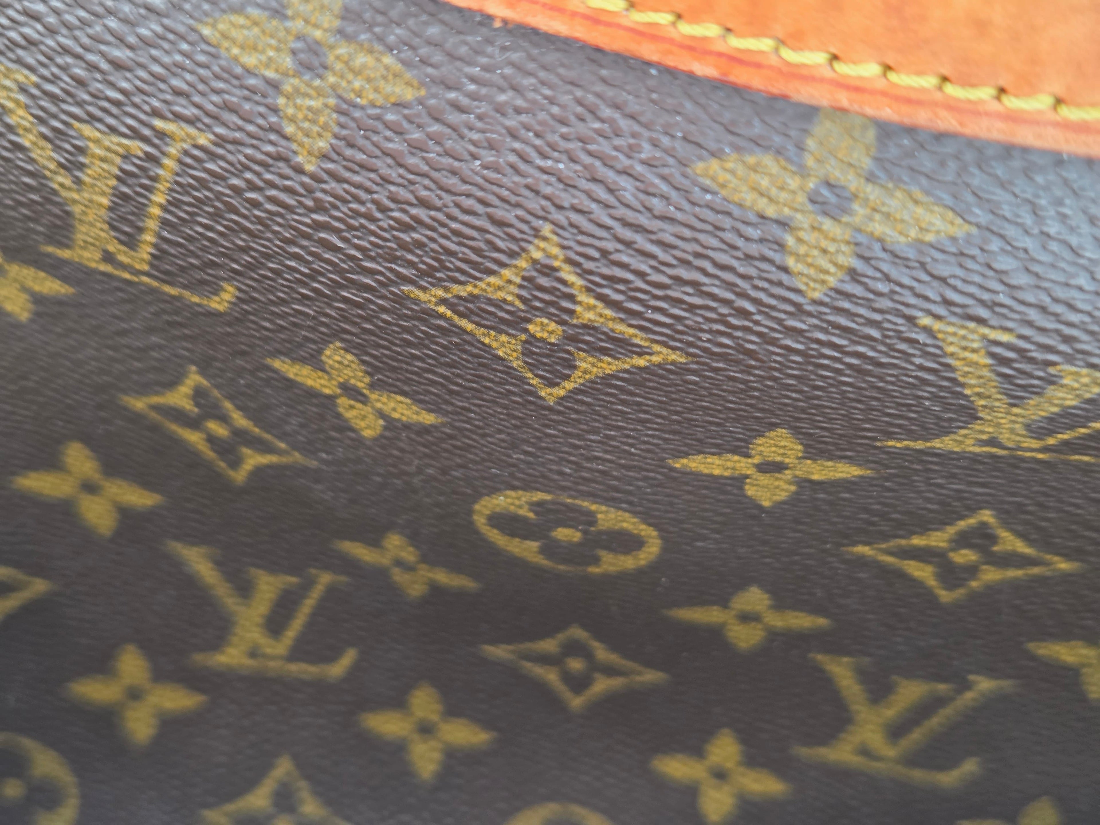 Close-up of Louis Vuitton monogram canvas in dark brown with gold-tone printed monogram motifs and a sliver of tan leather trim at the bottom.