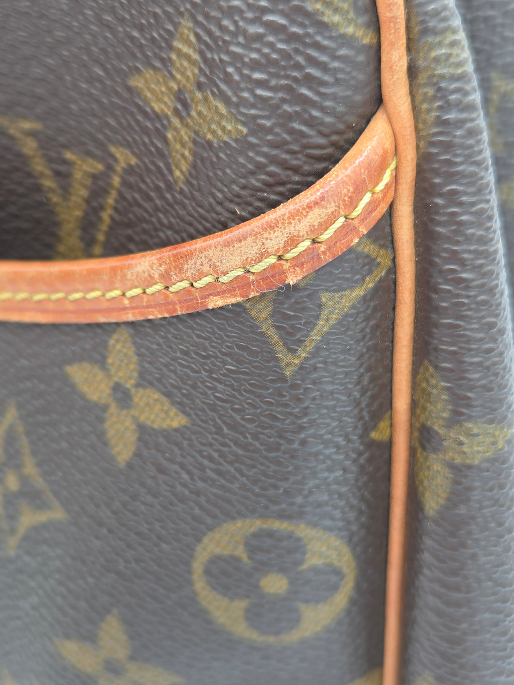 Close-up detail of a Louis Vuitton monogram canvas bag with a tan leather strap and yellow stitching.