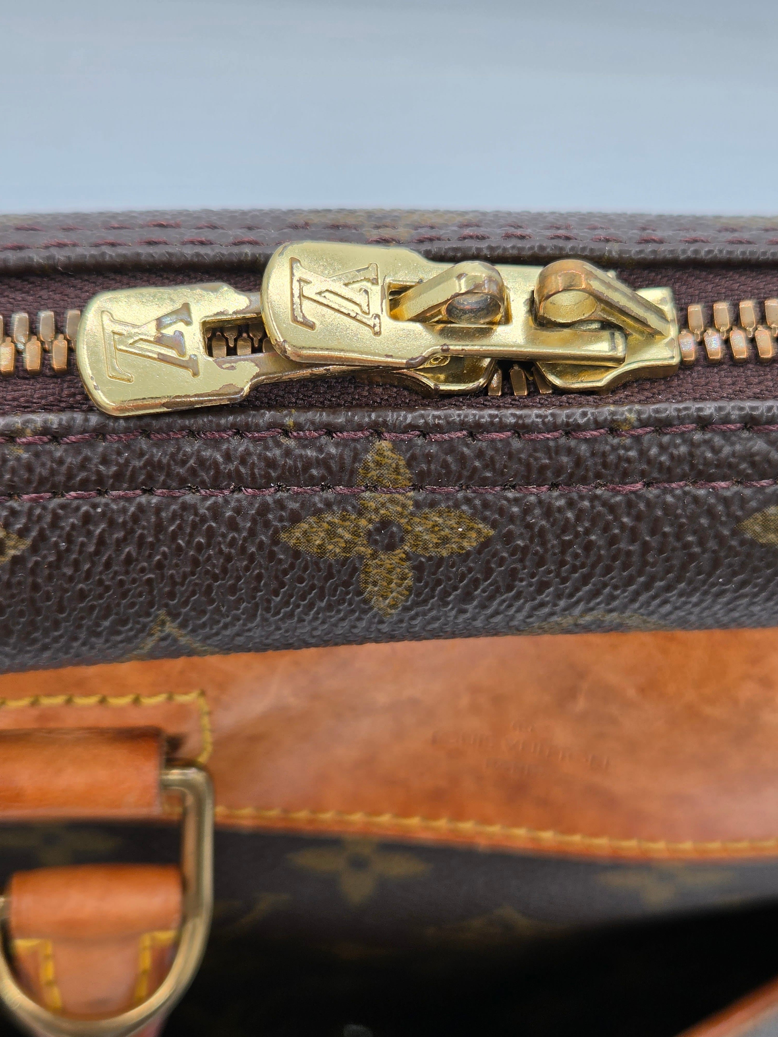 Close-up of a Louis Vuitton monogram canvas bag with a gold-tone metal zipper pull and brown leather trim.