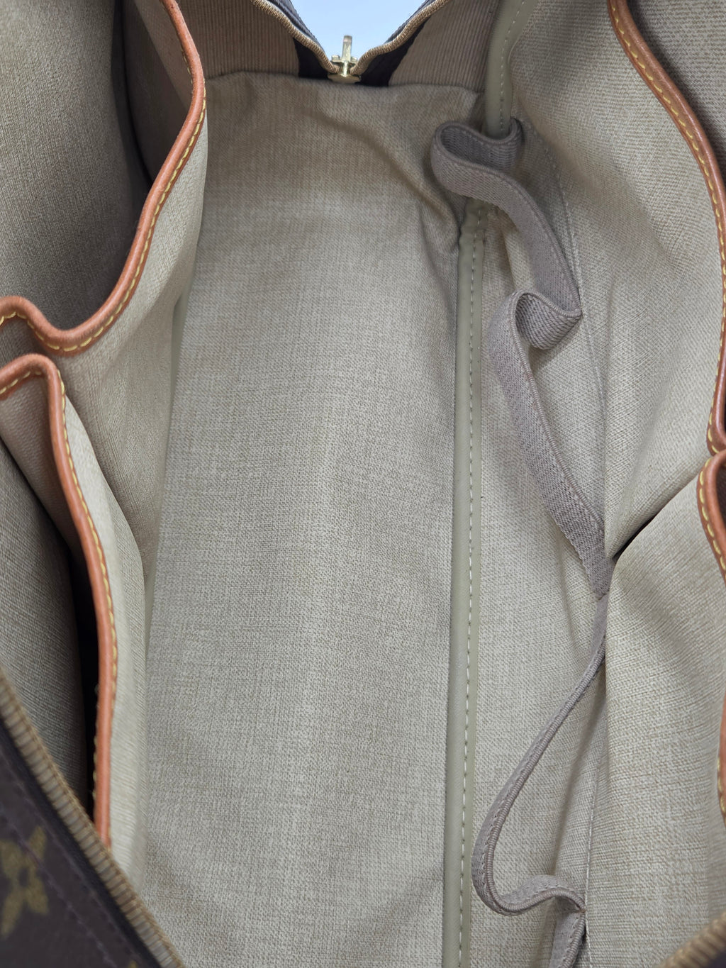 Close-up of the interior lining of a handbag, showing a light beige canvas body with tan leather trim and a gray fabric loop.