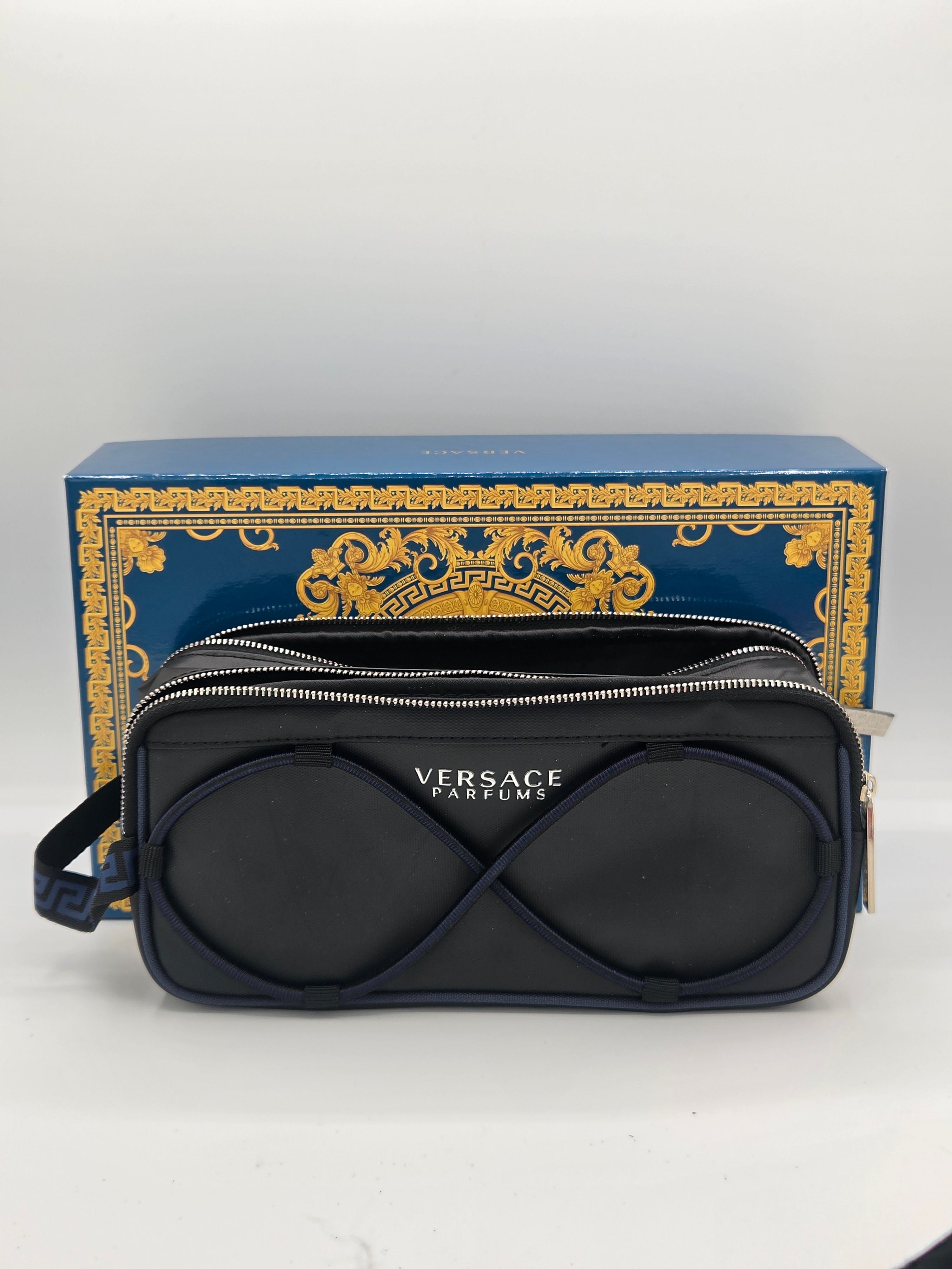 A Versace Cosmetics zippered pouch with the brand's infinity logo in black leather, displayed in front of its blue and gold branded box.