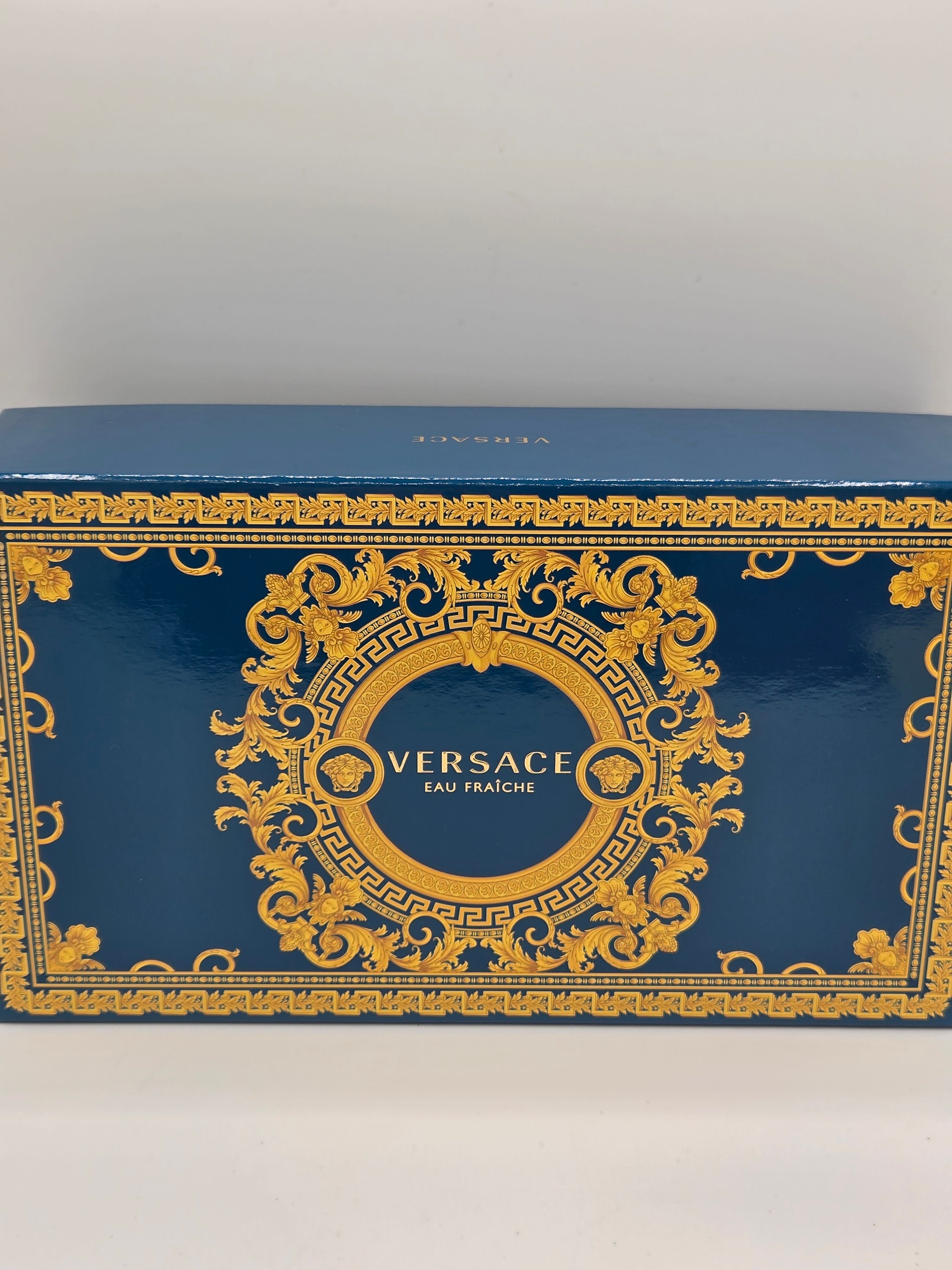 A blue and gold Versace Eau de Toilette box with ornate baroque-style gold detailing on a blue background, photographed against a plain light background.