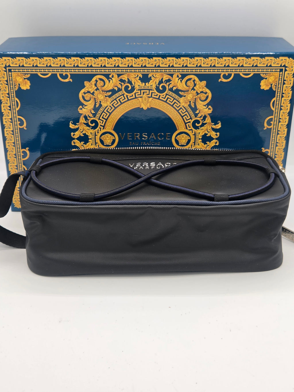 Black Versace leather pouch with a zippered closure and a strap, displayed in front of its blue and gold branded box.