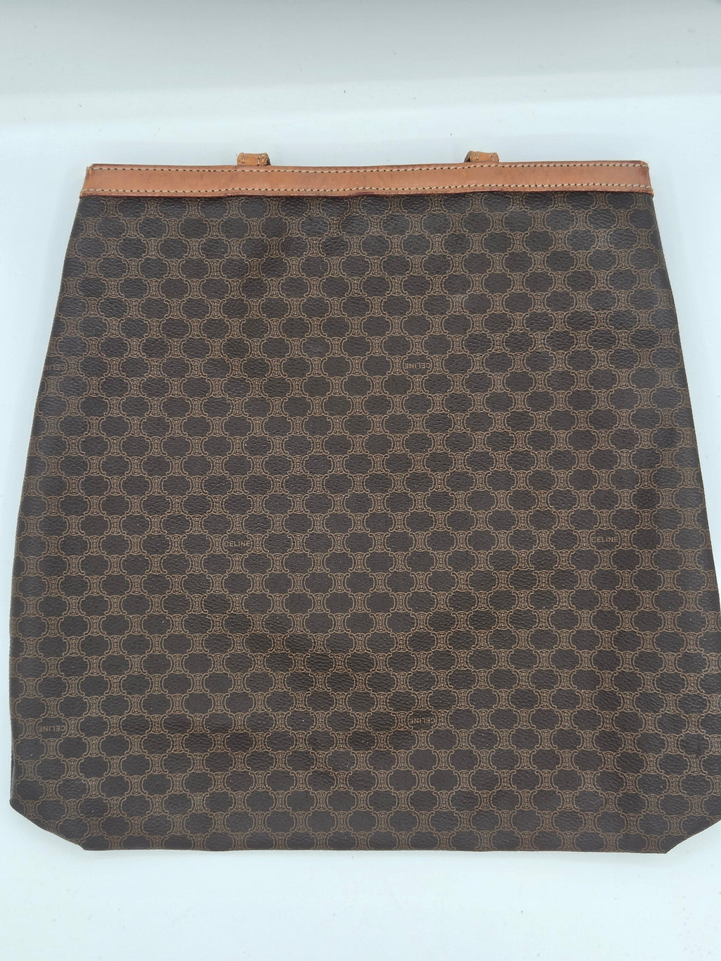 A brown and beige monogram canvas pouch with a tan leather trim on the left side, shown against a plain white background.