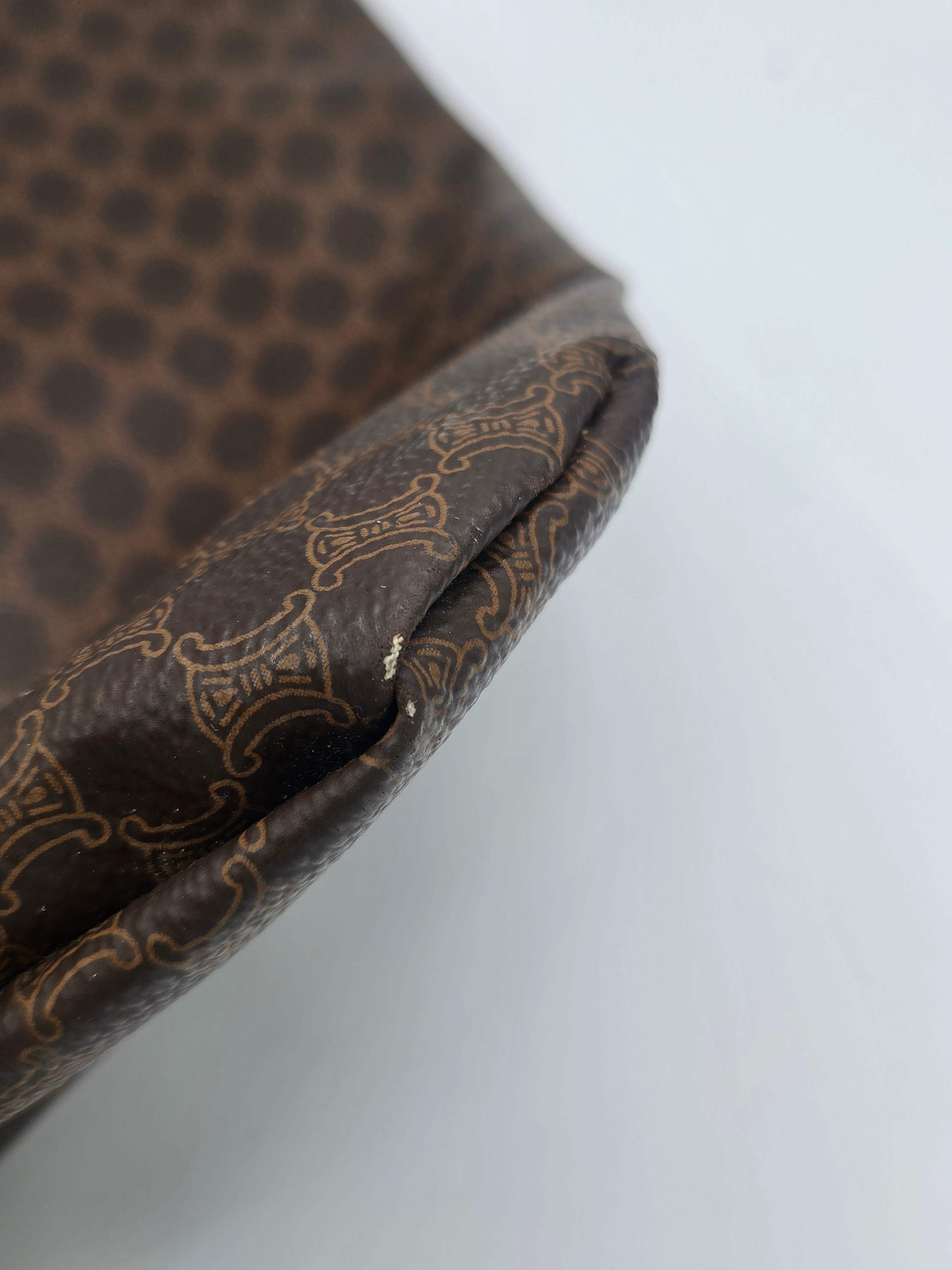 Close-up of a brown patterned fabric item, showing a dark brown surface with a repeating light beige ornamental pattern and a folded edge against a plain light background.