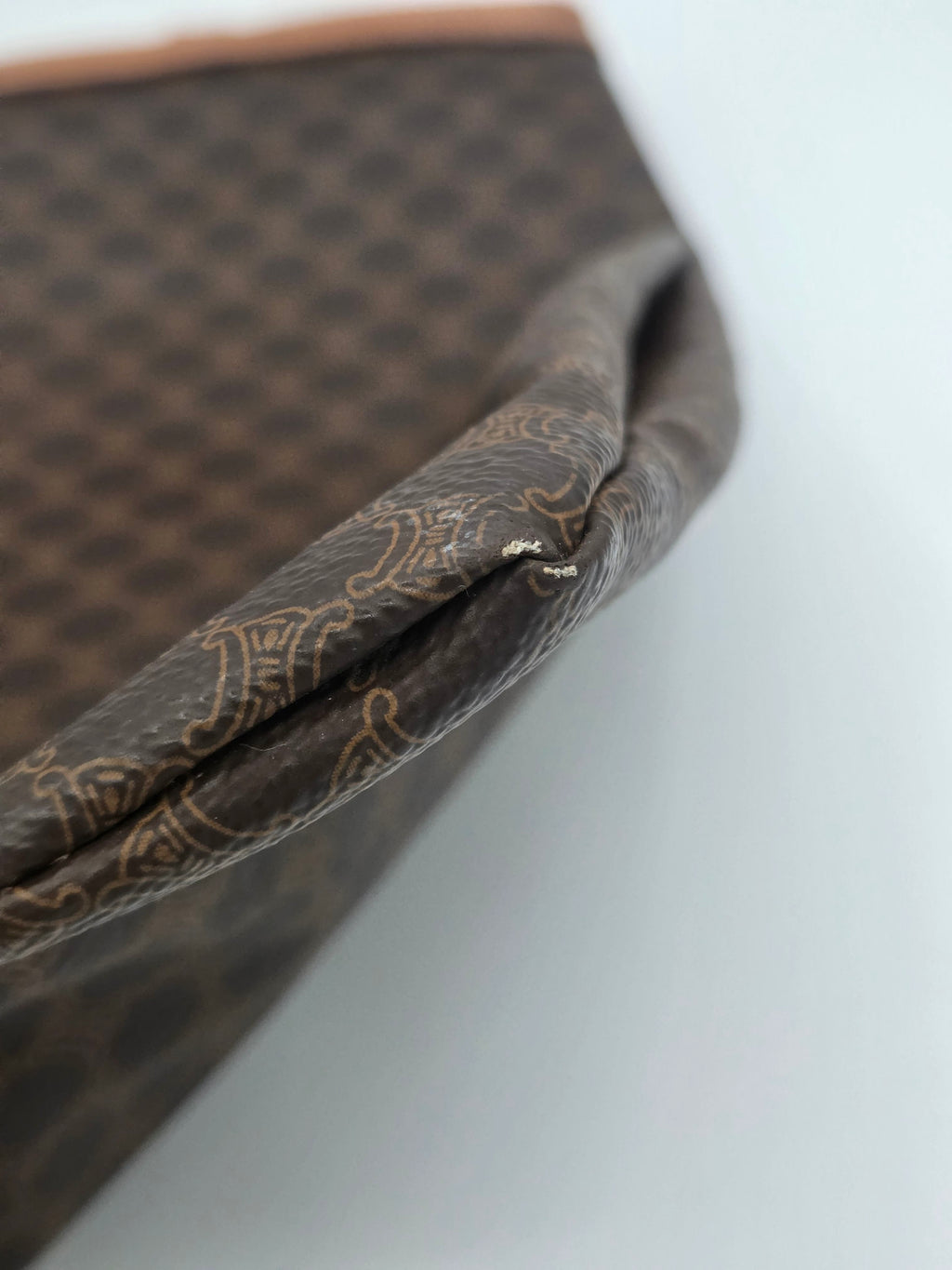 Close-up of a brown patterned fabric accessory, showing a folded corner with a small metallic rivet on a plain light background.