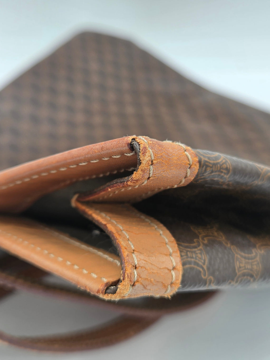 Close-up of a brown patterned leather bag corner with tan leather trim and visible wear on the edge.