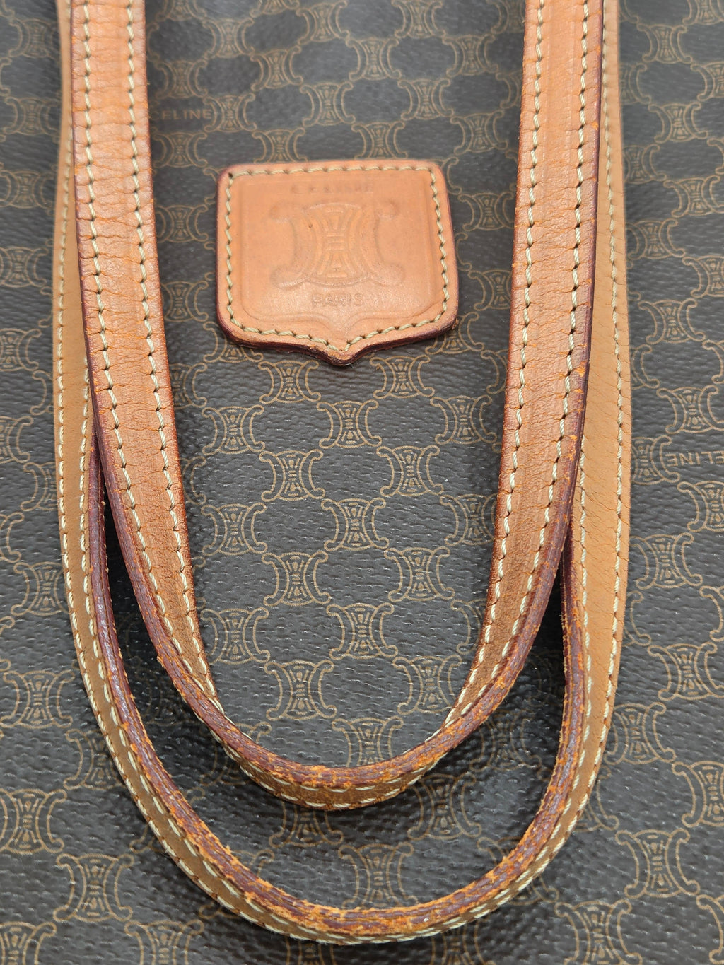 Close-up of a Louis Vuitton handbag strap made of tan leather with contrast stitching, resting on the brand's dark brown and beige monogram coated canvas.