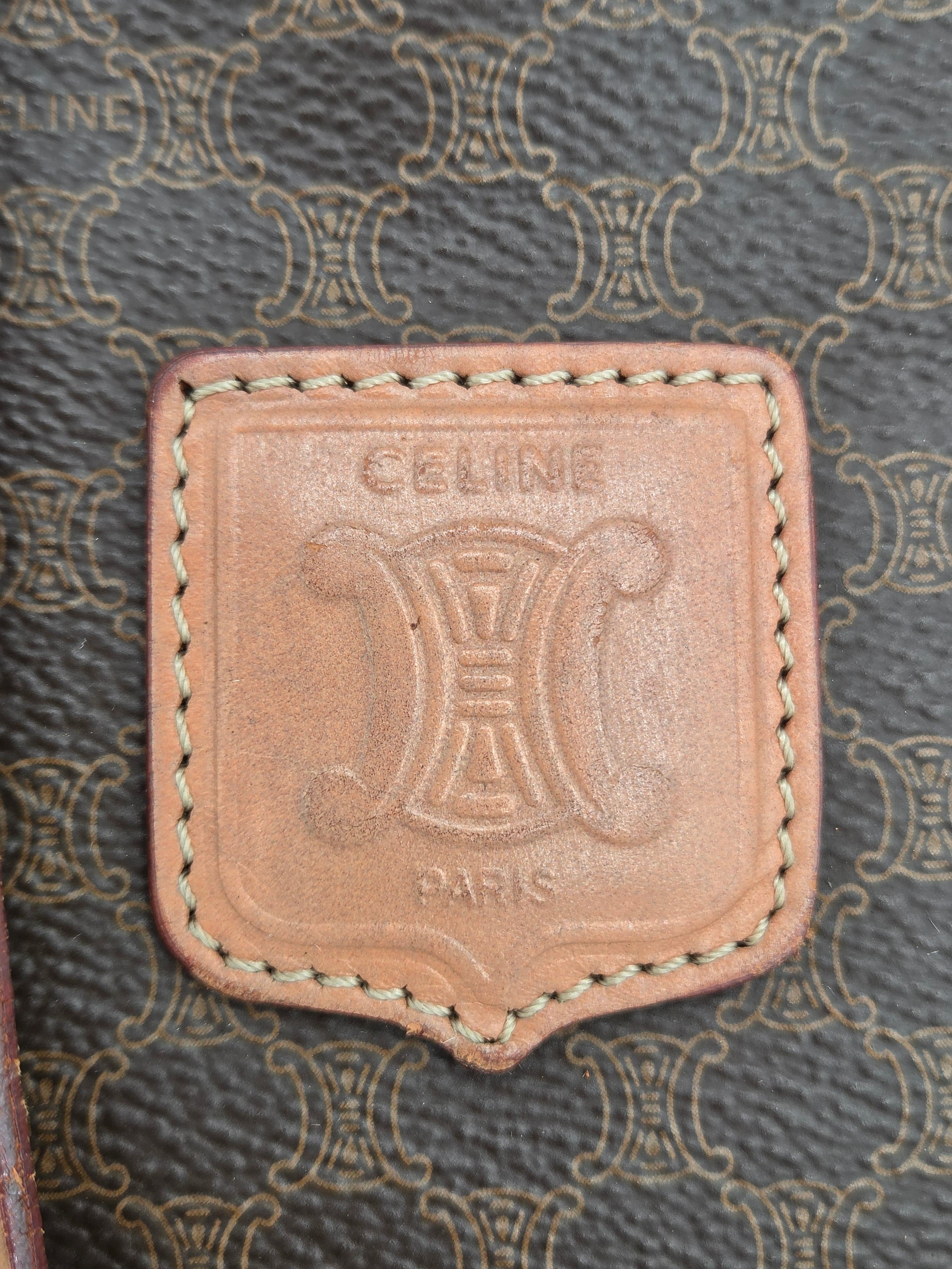 Close-up of a Celine leather patch with the brand's signature Triomphe logo and 'CELINE PARIS' text, set against a dark gray patterned background.