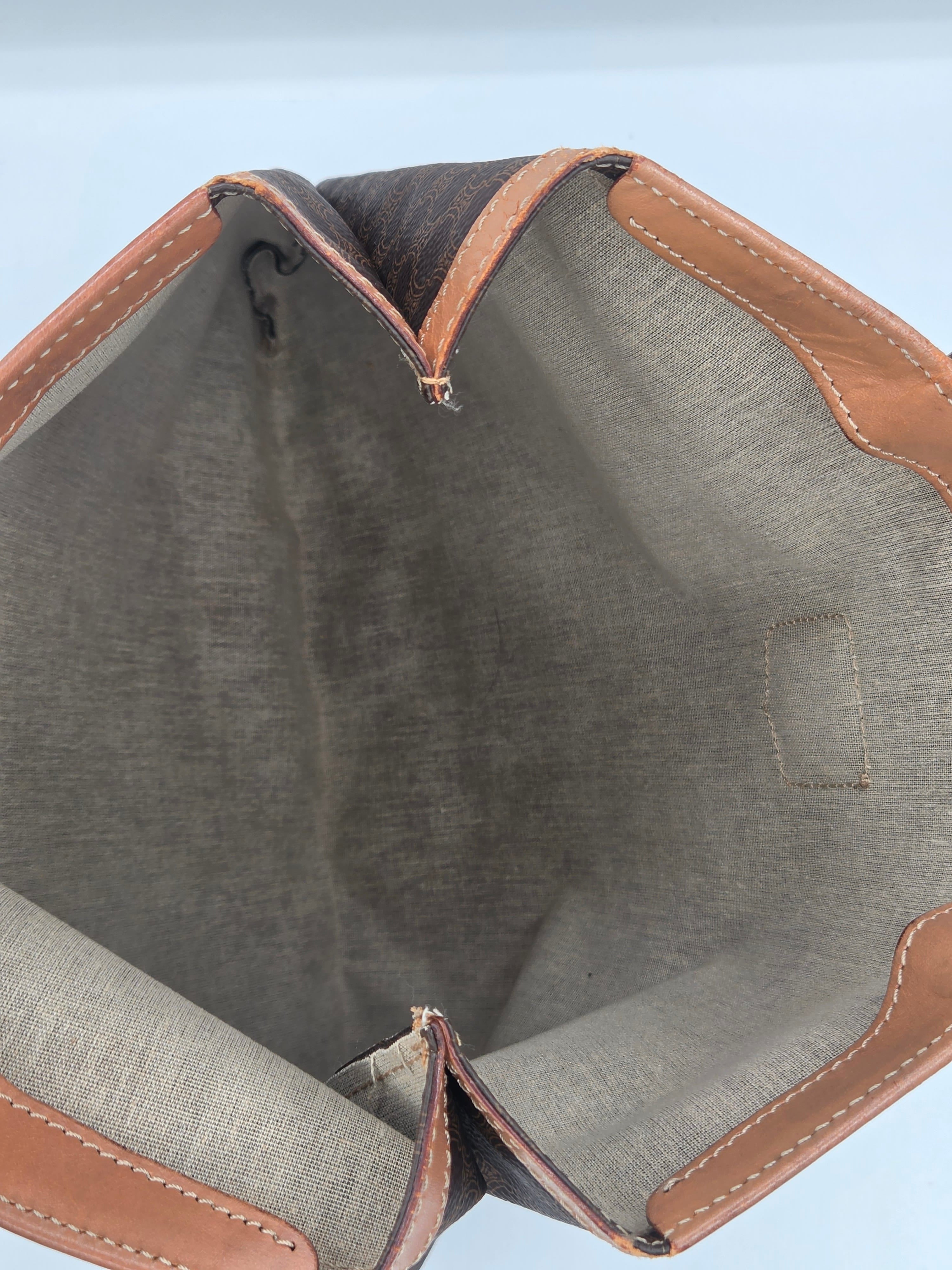 Close-up view of the interior of a handbag, showing a gray woven fabric lining with tan leather trim and stitching.