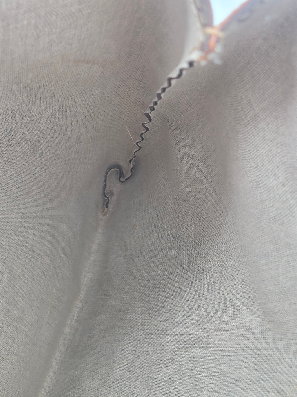 A close-up of a light gray fabric surface with a small dark metallic spiral-shaped defect or seam detail near the center-left.