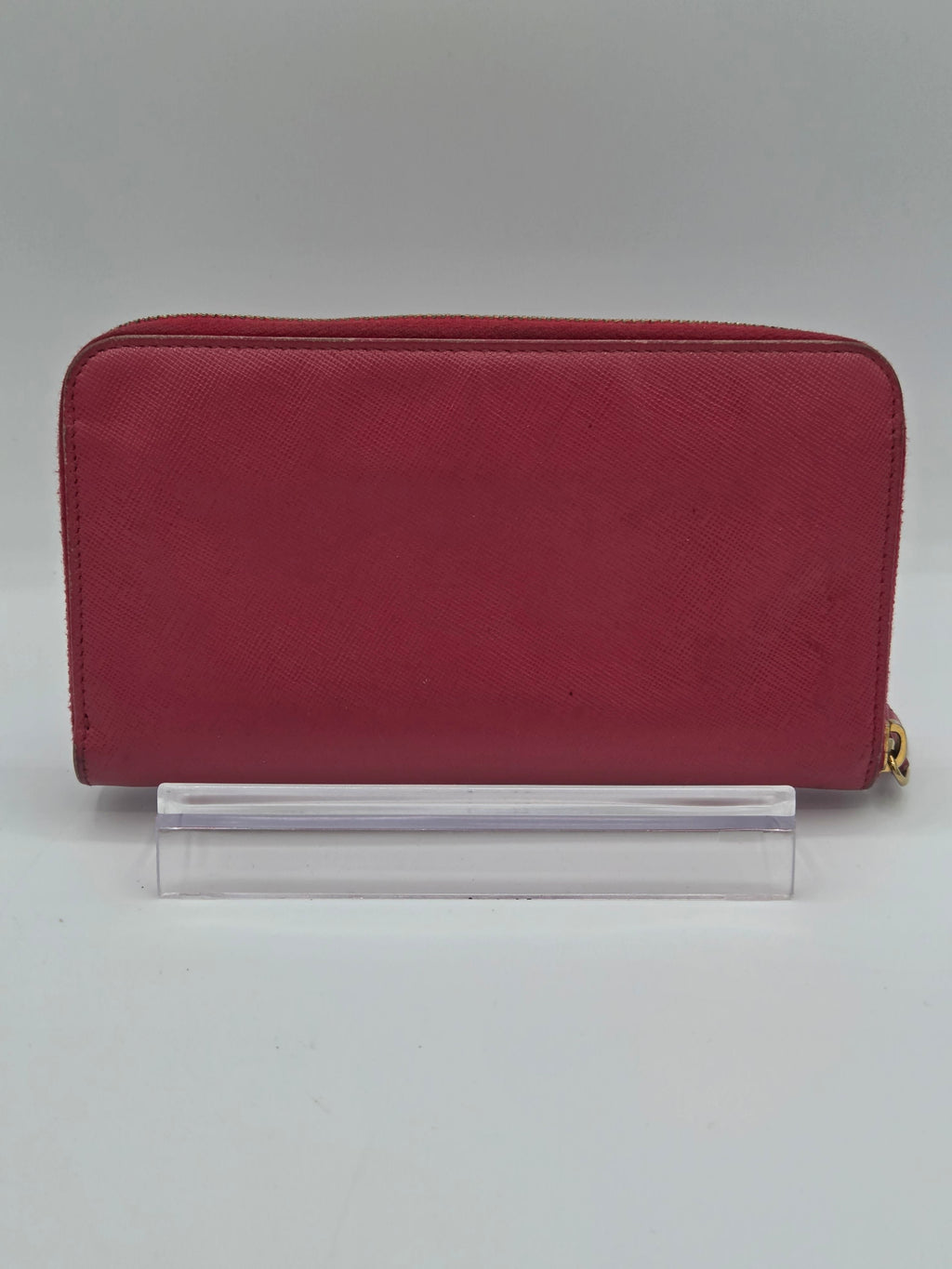A burgundy zip-around wallet with a gold zipper pull, shown standing vertically next to a clear acrylic block on a light gray background.
