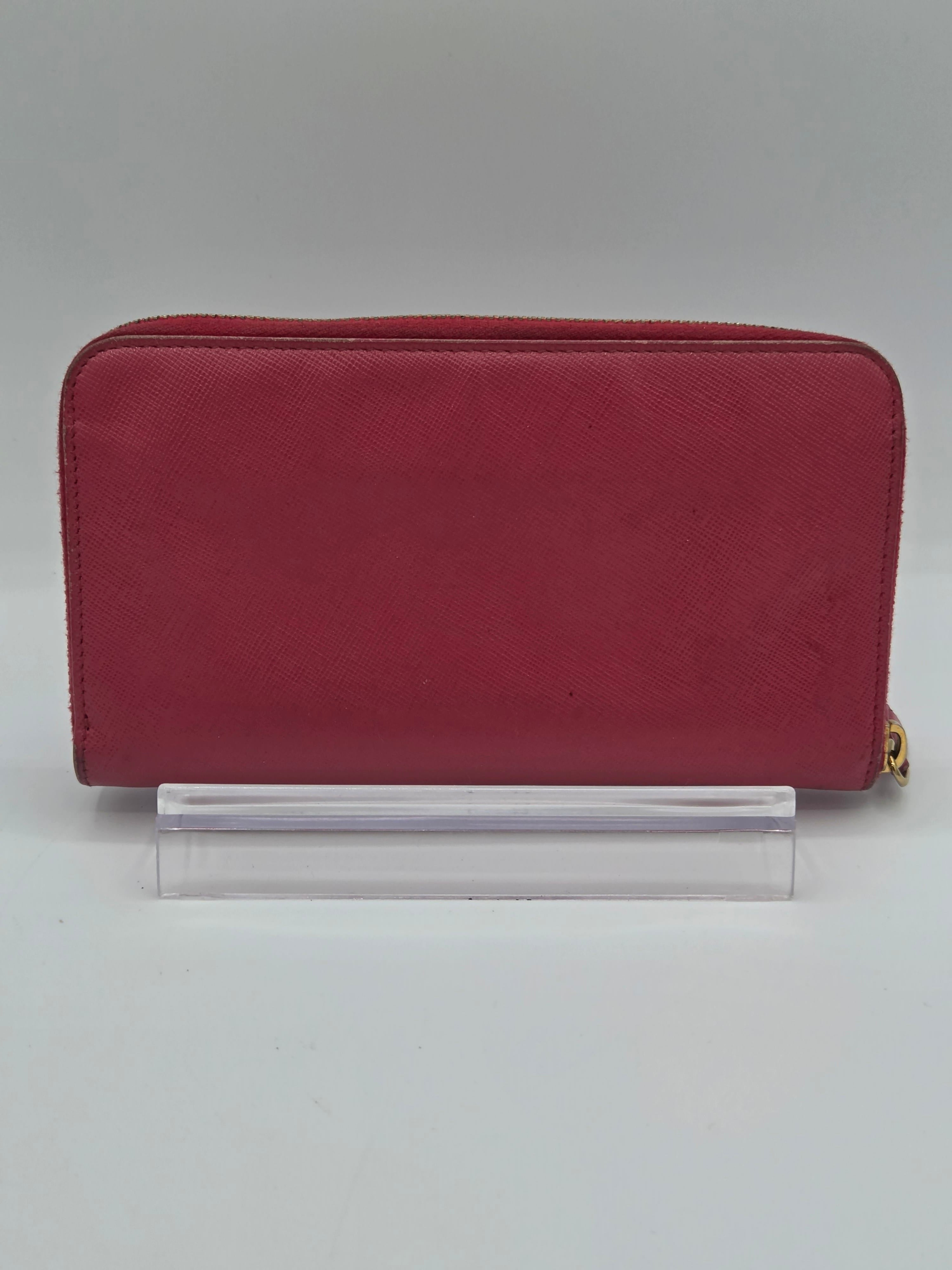 A burgundy zip-around wallet with a gold zipper pull, shown standing vertically next to a clear acrylic block on a light gray background.