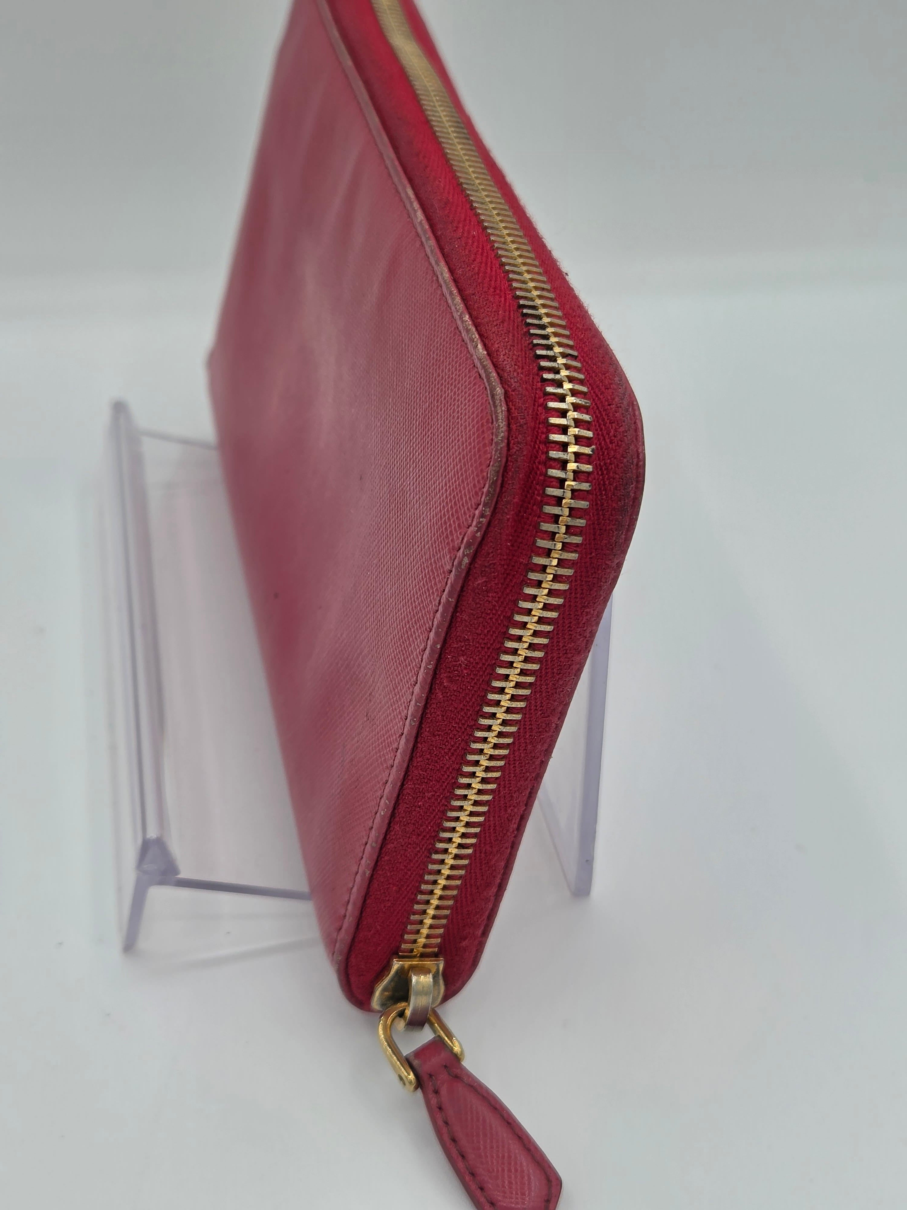 A red leather zip-around pouch with a gold-tone zipper and pull tab, displayed on a clear acrylic stand against a white background.