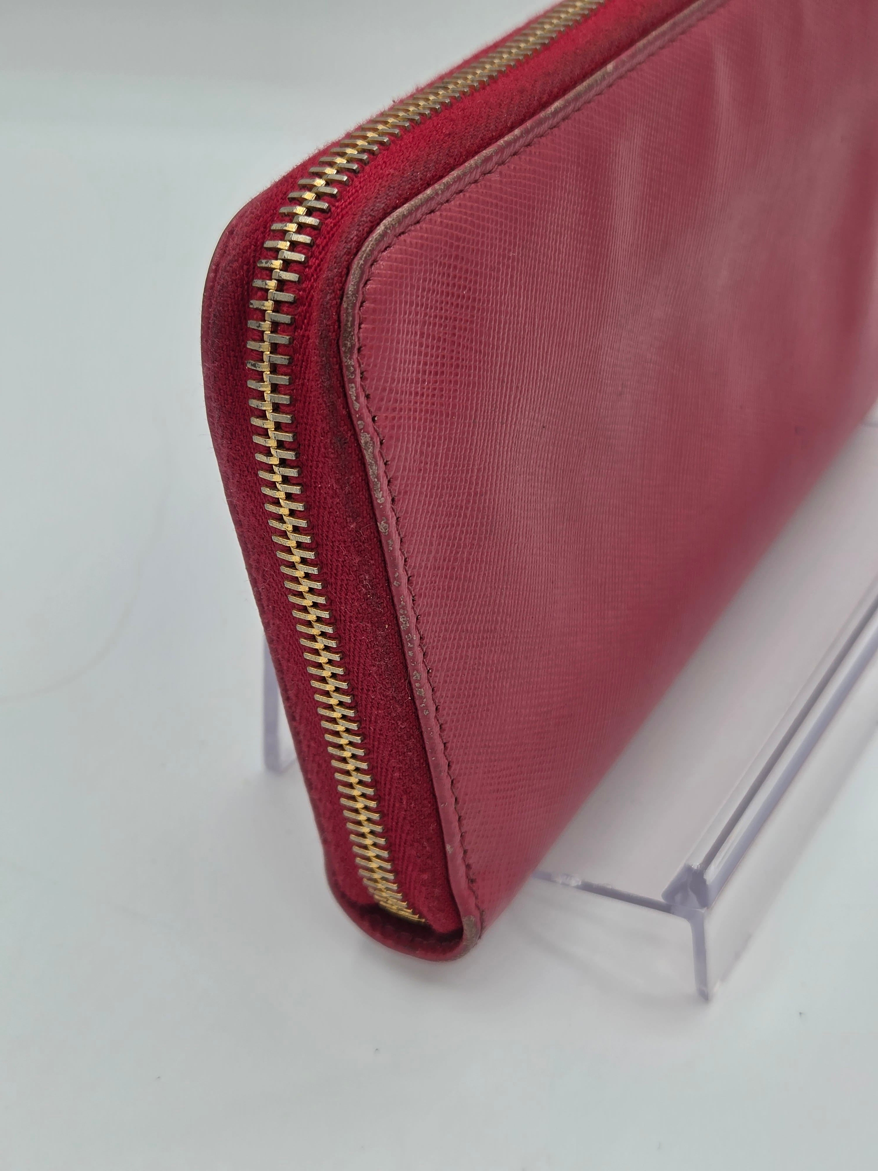 A close-up of a burgundy leather zip-around wallet with a gold zipper, resting on a clear acrylic display stand against a white background.