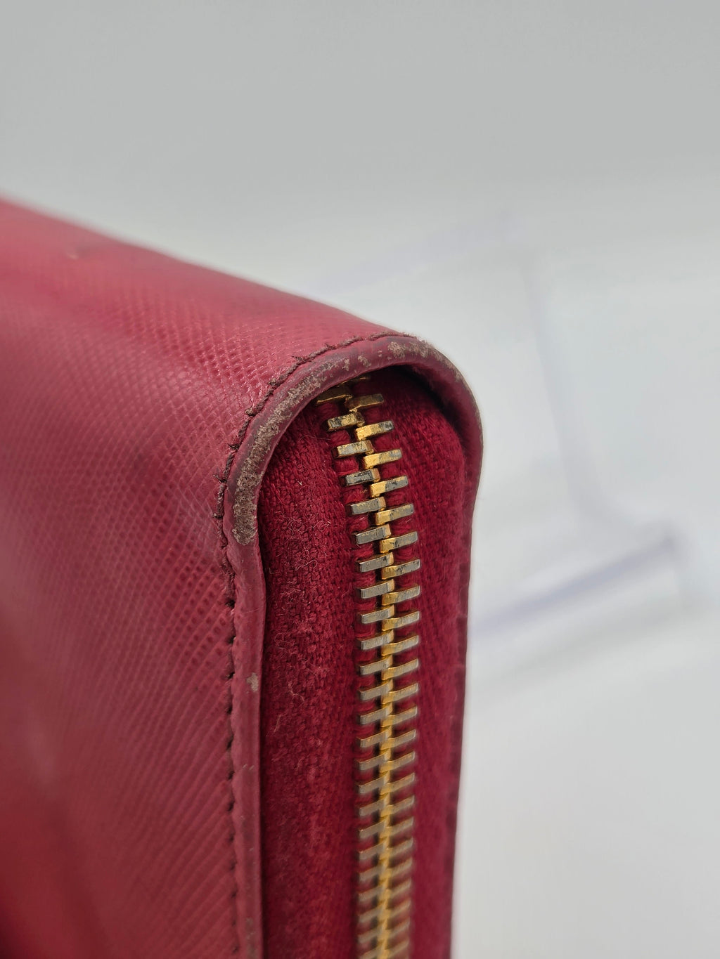 Close-up of a burgundy textured leather zippered pouch showing the gold-tone zipper and stitching.