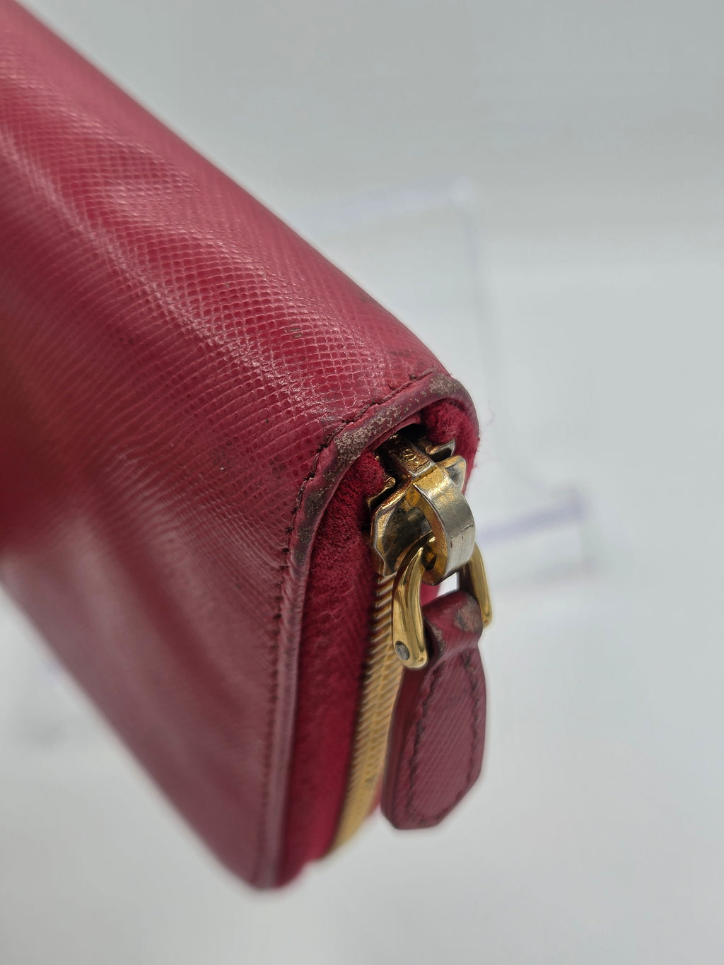 A close-up of a burgundy leather zip-around wallet with a gold-tone metal zipper pull, showing the textured leather grain and hardware against a light background.