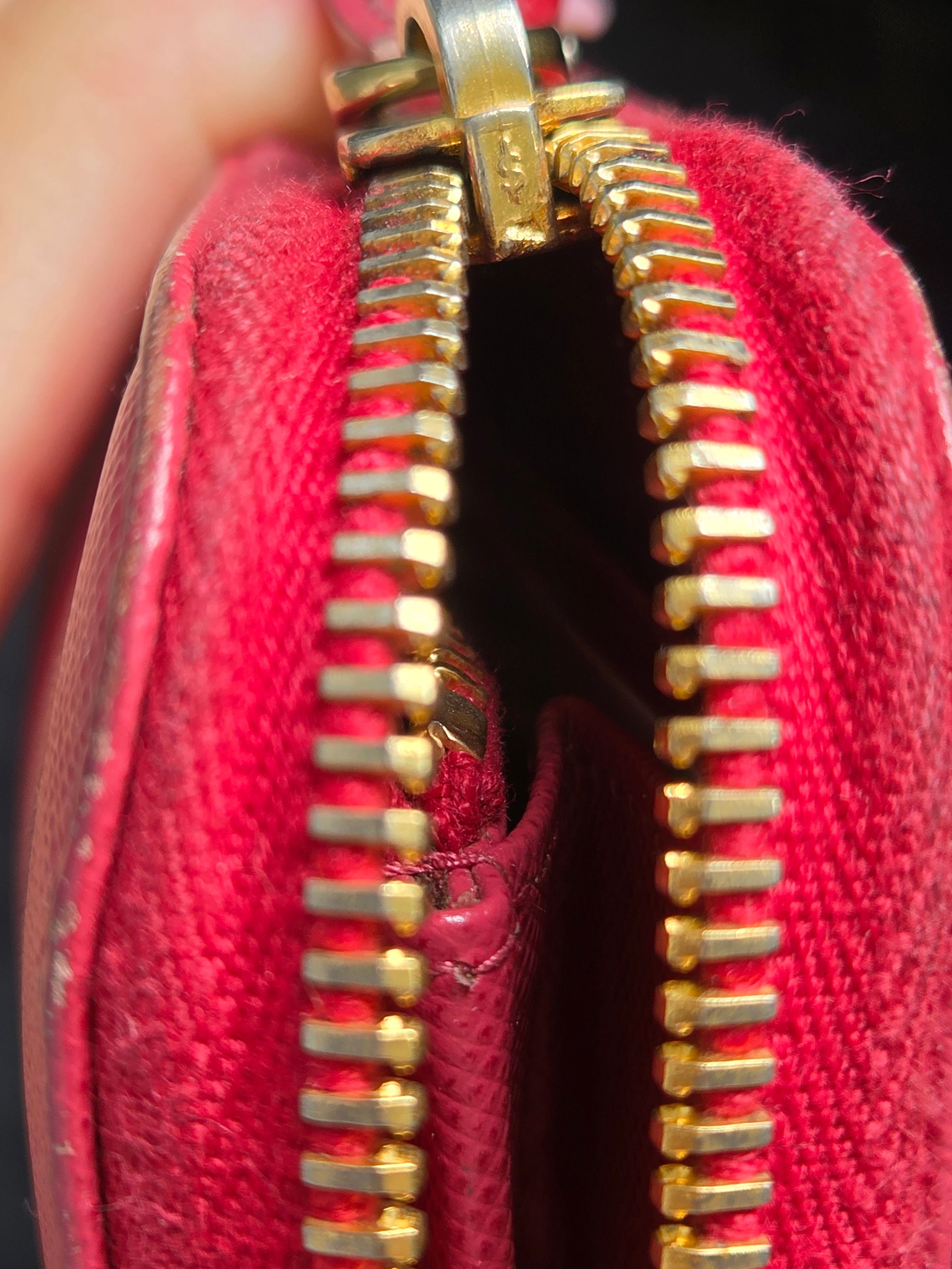 Close-up of a red fabric zippered pouch or wallet with gold-tone metal zipper teeth, held open by a hand.