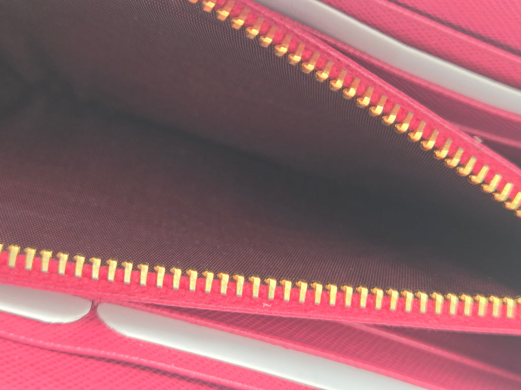 Close-up of a pink textured wallet or clutch showing the interior lining, a gold zipper, and part of a white card slot.