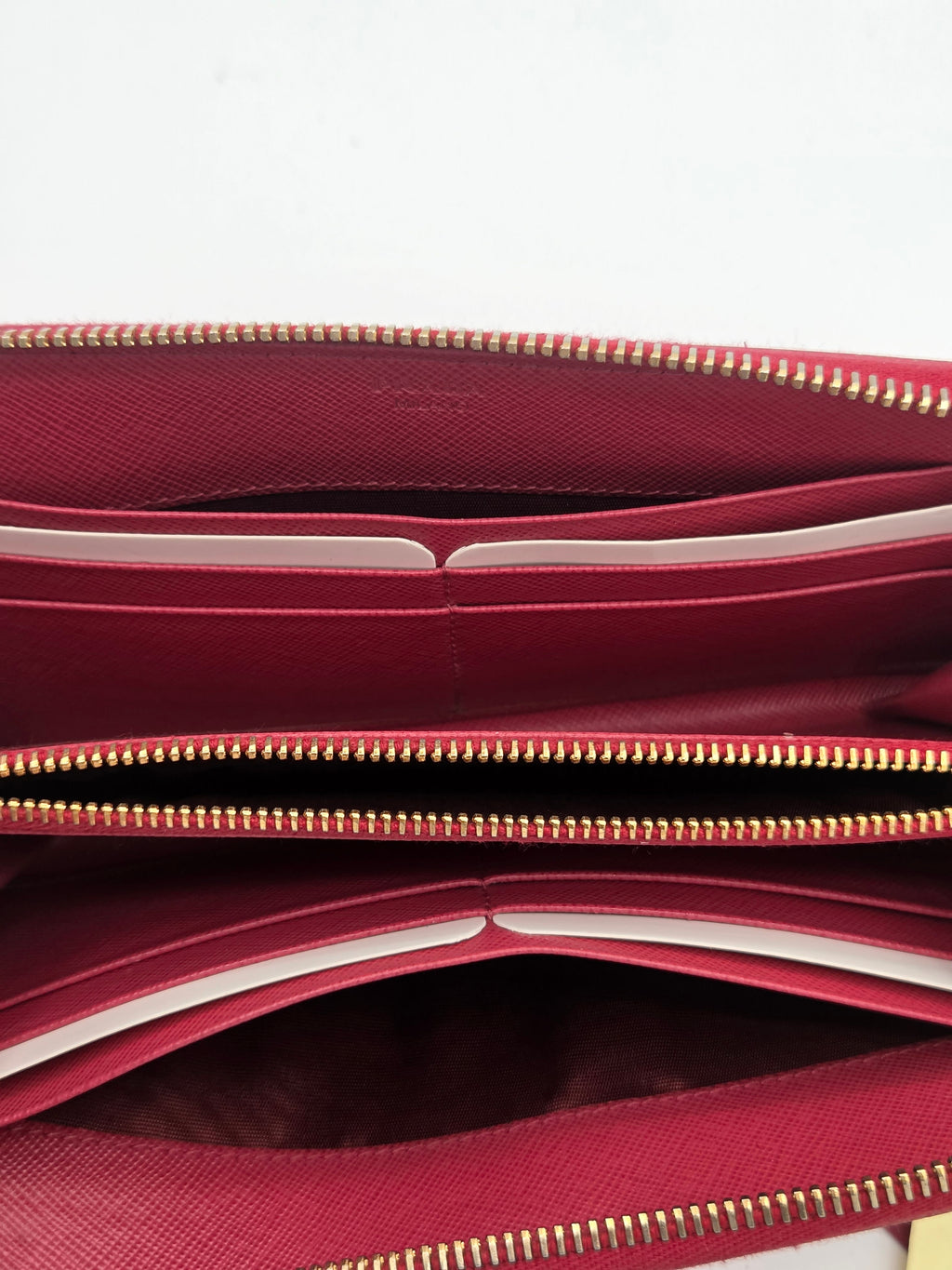 Close-up of a burgundy leather wallet or clutch showing the interior compartments, gold-tone zippers, and card slots against a white background.