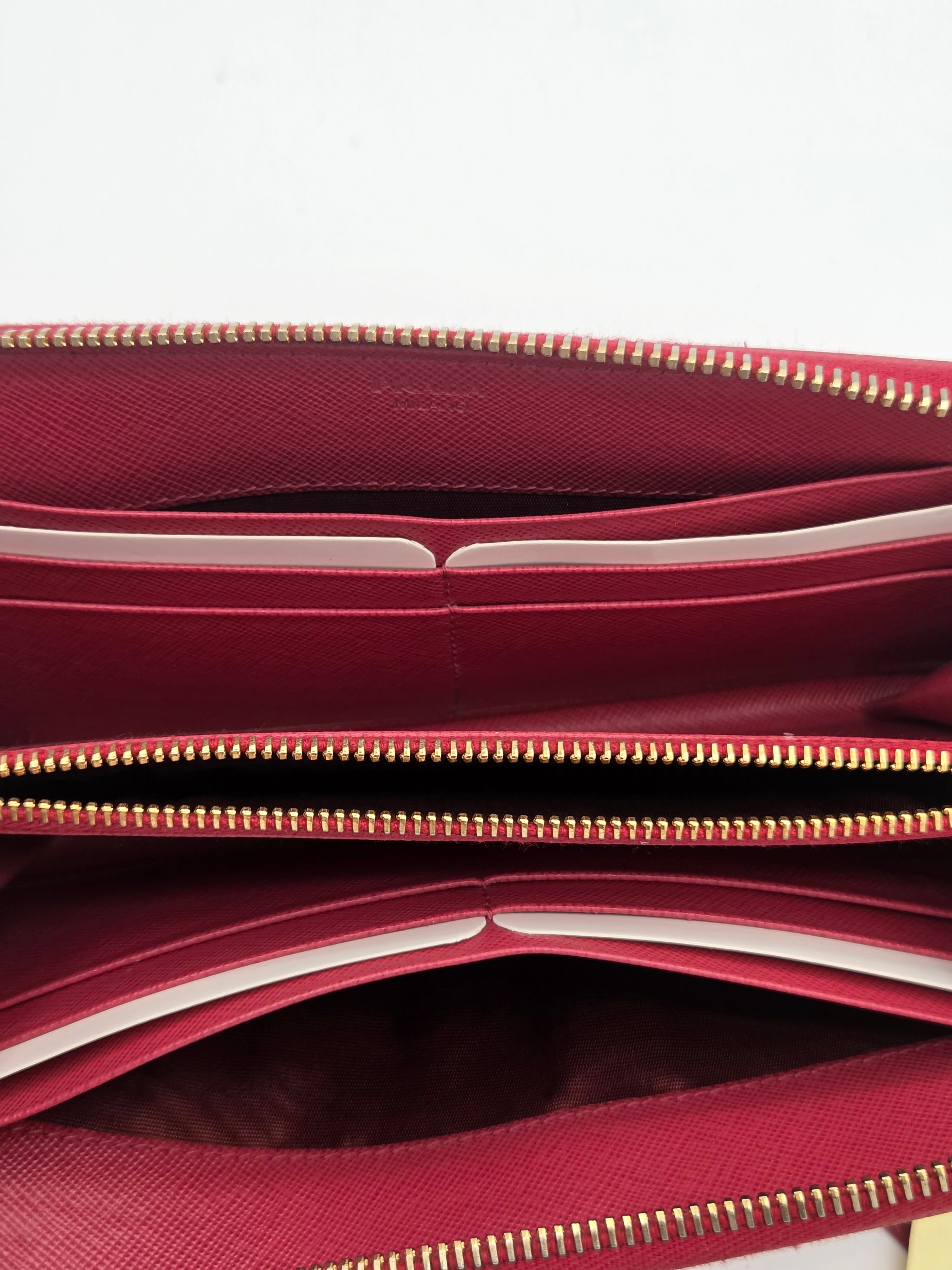 Close-up of a burgundy leather wallet or clutch showing the interior compartments, gold-tone zippers, and card slots against a white background.