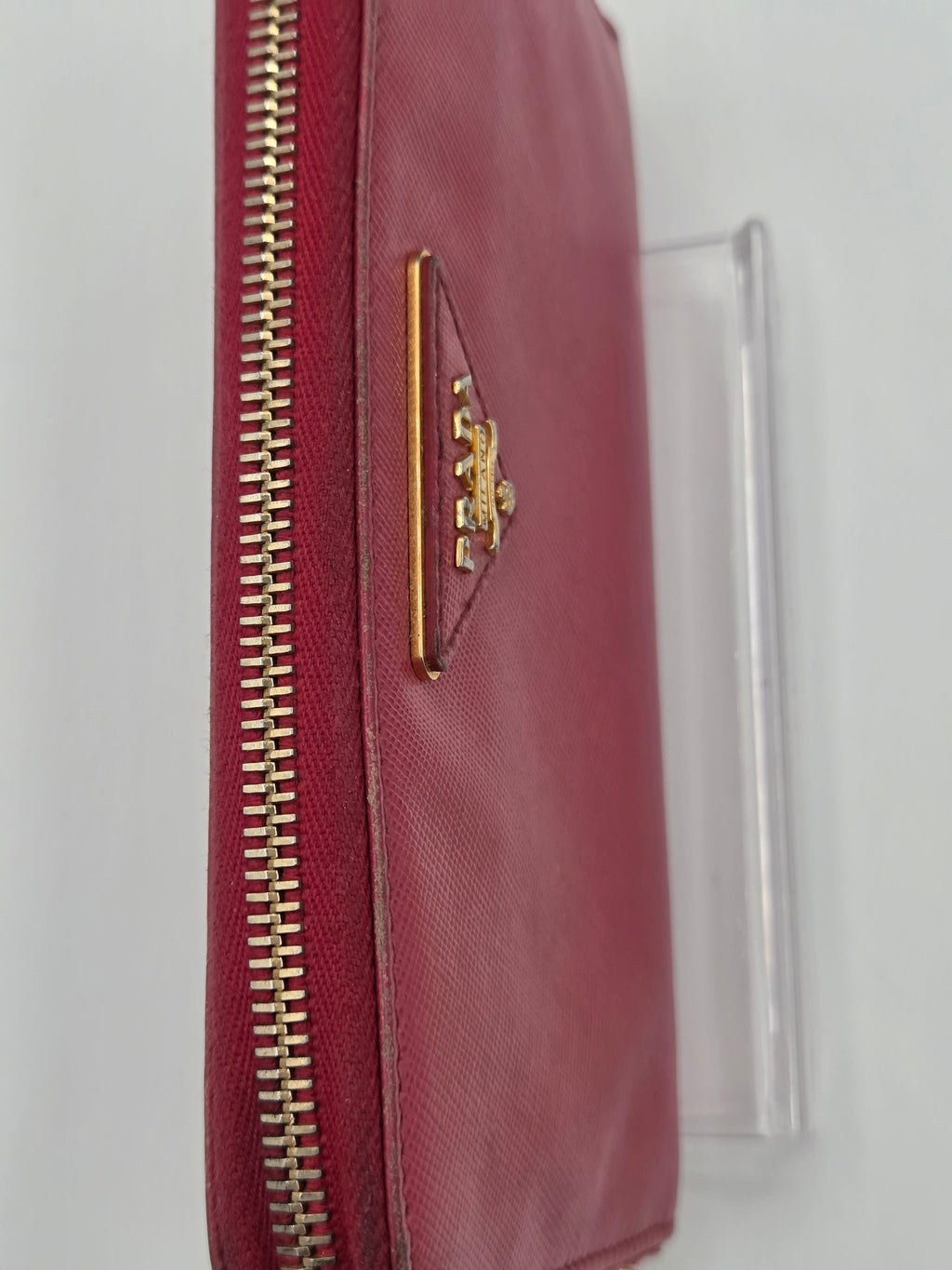 A burgundy leather zip-around wallet with a gold-tone metal zipper and a triangular gold-tone logo plaque on the front, shown against a plain light background.
