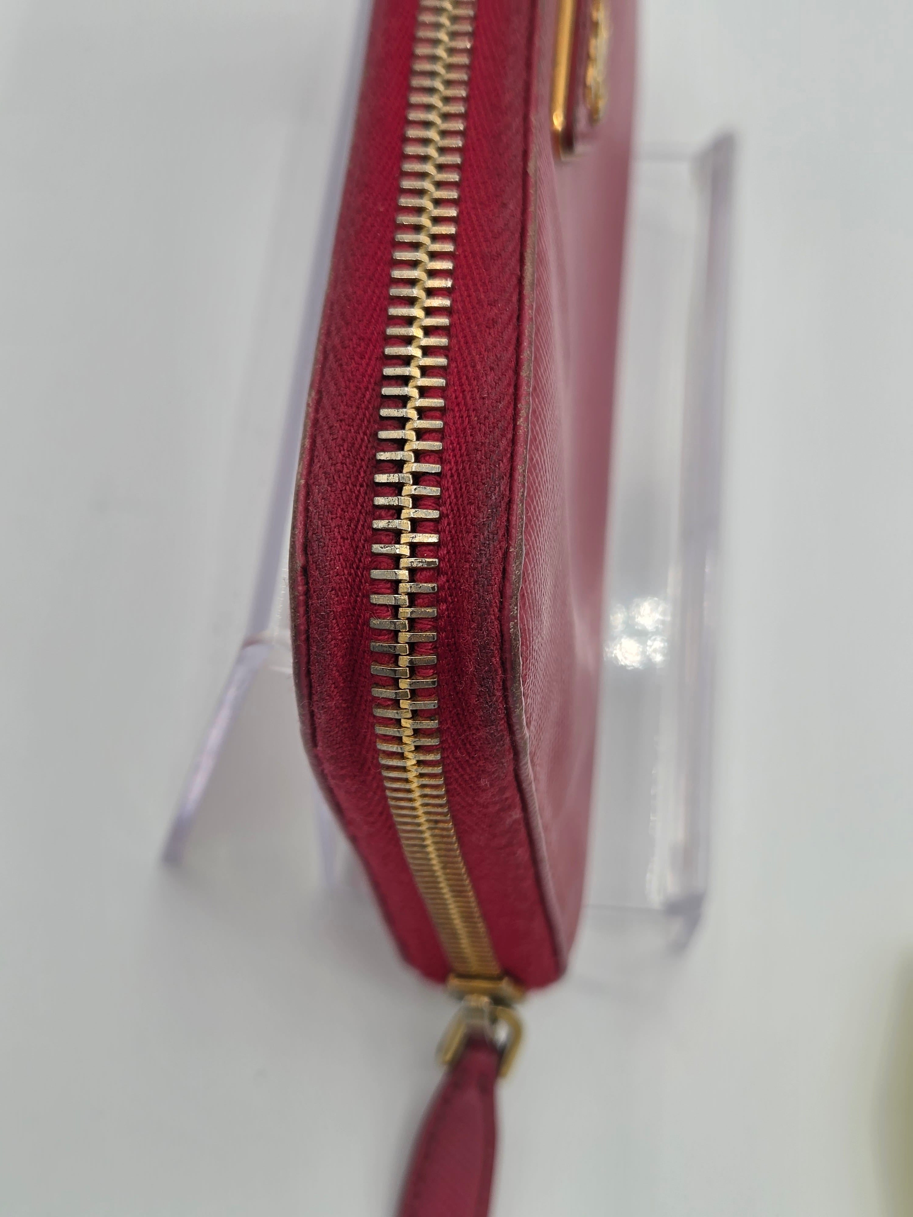 A close-up of a burgundy leather zip-around wallet with gold-tone hardware, resting on a clear display stand against a white background.