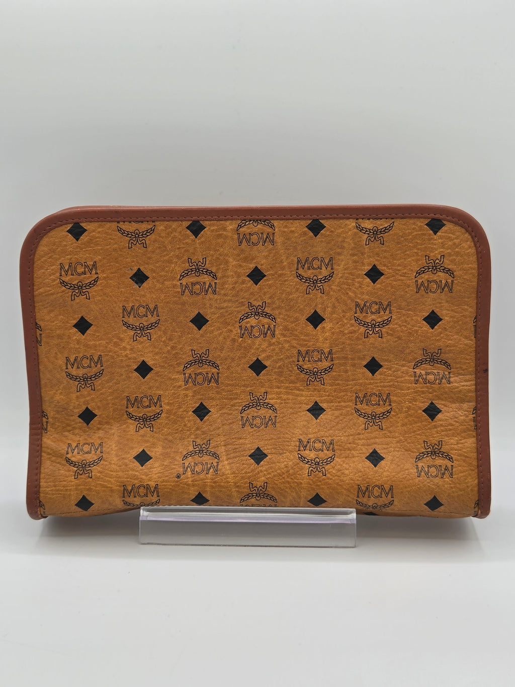 A brown MCM monogram zip-around pouch or organizer case with a clear plastic side clip, shown against a plain light gray background.