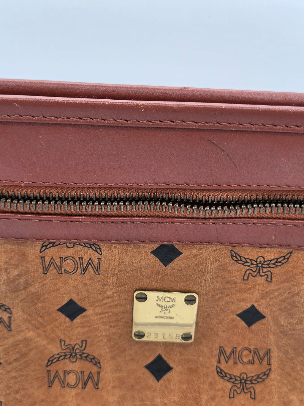 Close-up of an MCM monogram canvas bag in brown with a reddish-brown leather trim and a gold-tone metal plaque.